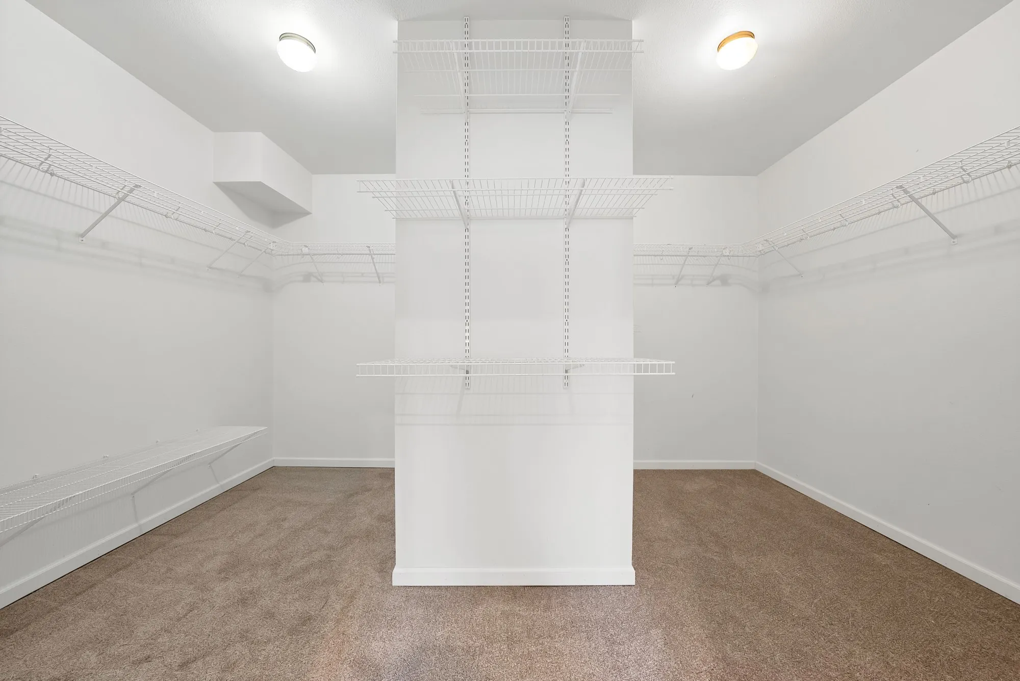 Recessed lighting illuminates a carpeted floor, featuring extensive wire shelving and a built-in bench