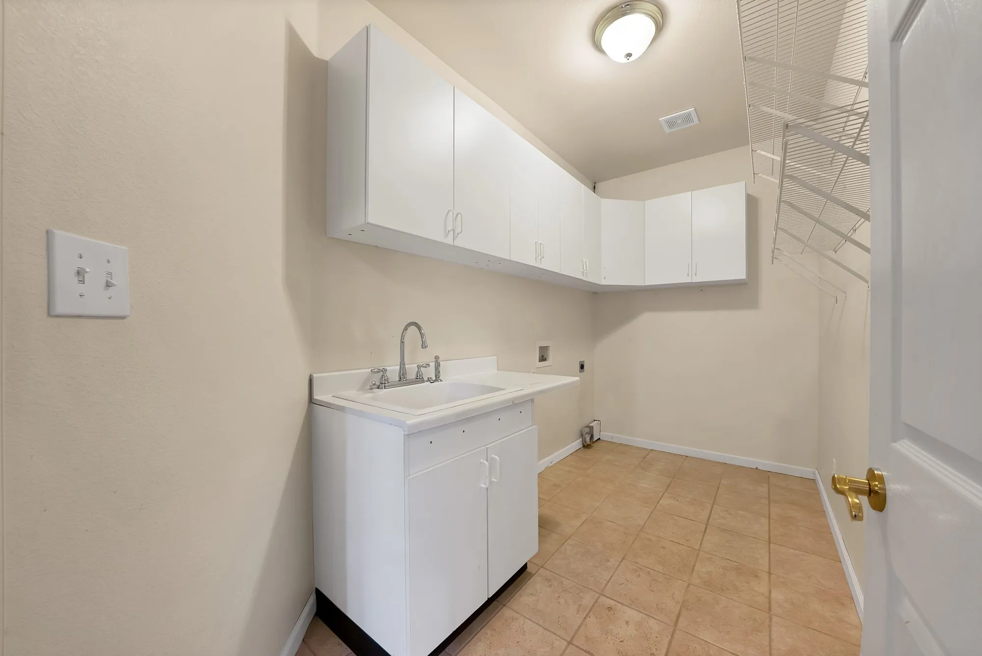 Utility room featuring a built-in sink with cabinetry, overhead white cabinetry, and tile flooring