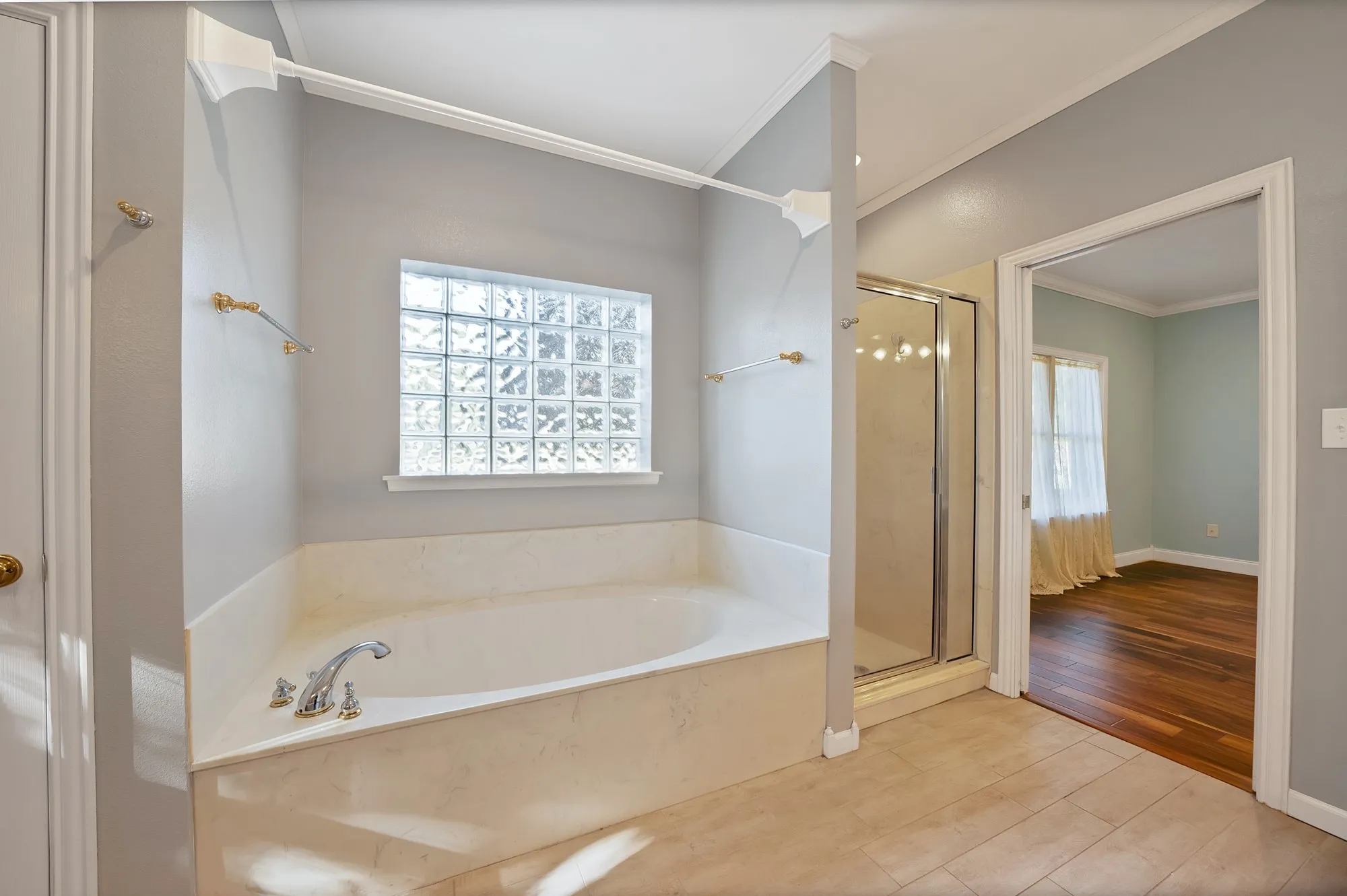 Soaking tub with chrome fixtures, glass block window, tile flooring, and a glass-enclosed shower