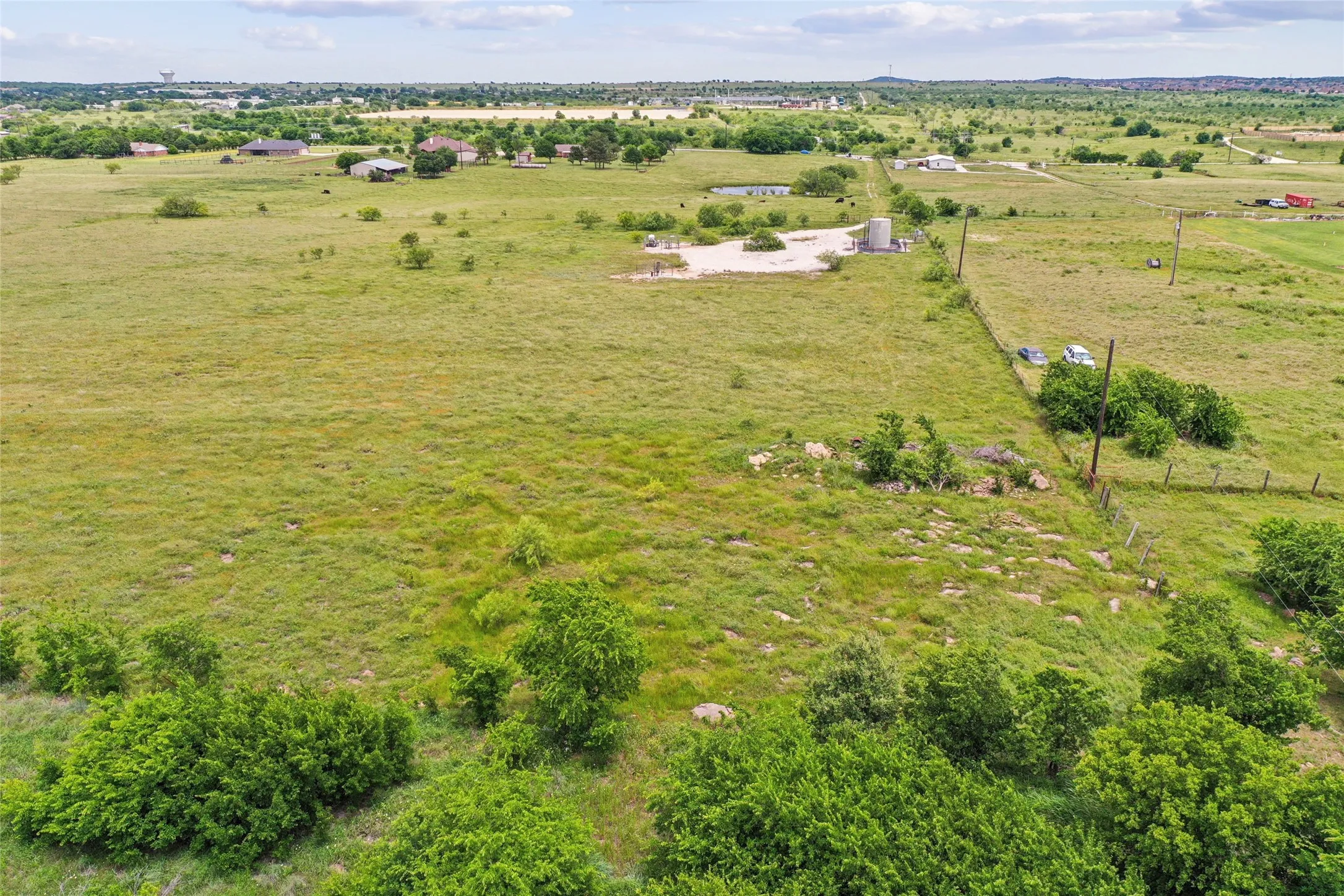 Expansive open land with varied topography, scattered trees, and distant structures