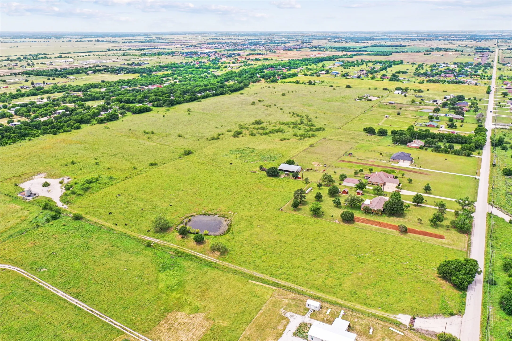 Expansive green landscape with scattered trees, a visible pond, and a defined roadway