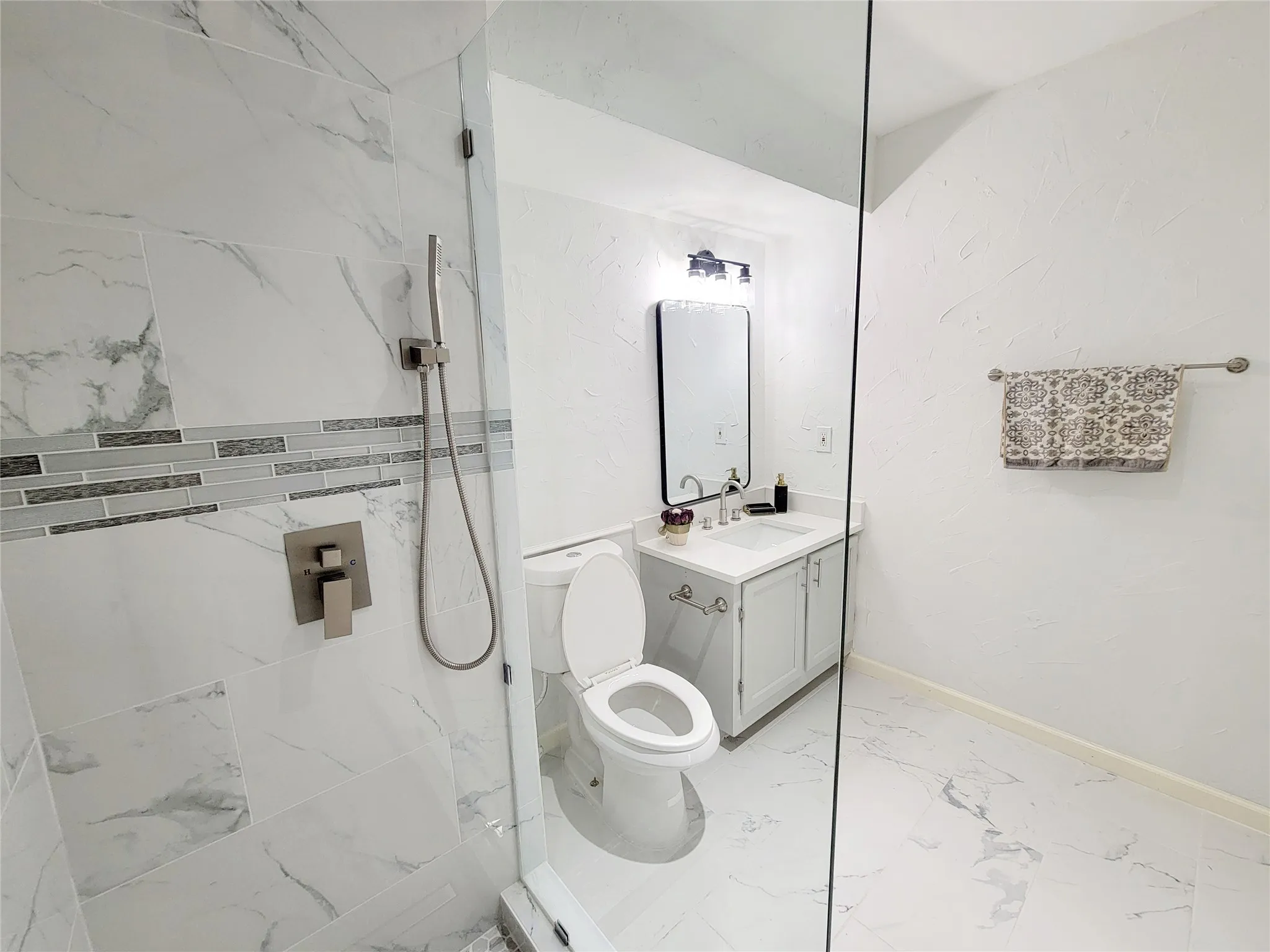 Bathroom with vanity, toilet, baseboards, marble finish floor, and a walk in shower