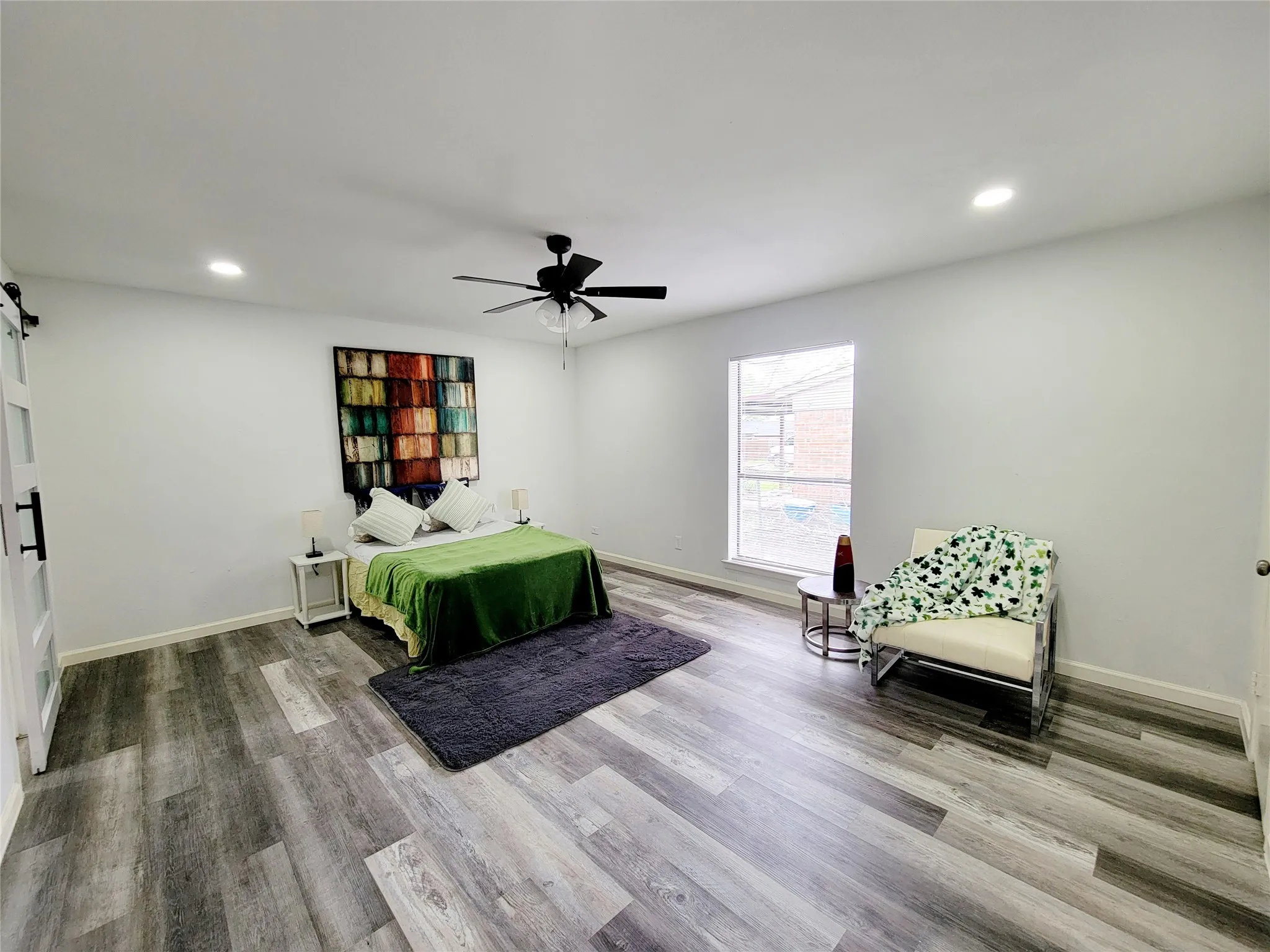 Bedroom with baseboards, a barn door, wood finished floors, and recessed lighting