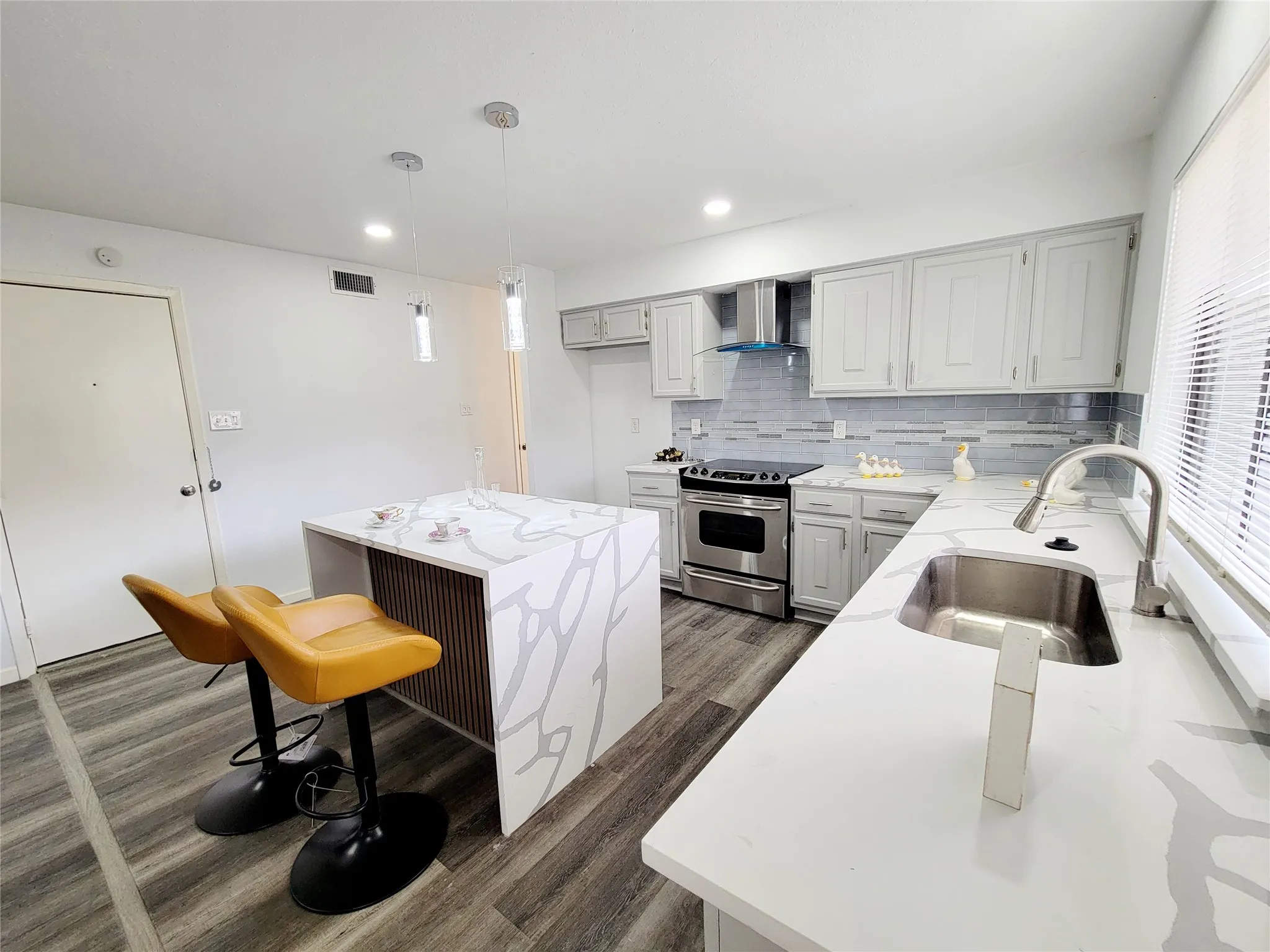 Kitchen with stainless steel range with electric stovetop, visible vents, a sink, wall chimney range hood, and backsplash