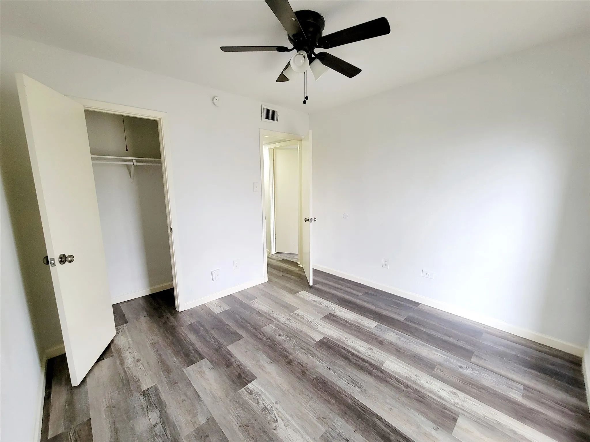 Unfurnished bedroom with a closet, visible vents, baseboards, wood finished floors, and a ceiling fan