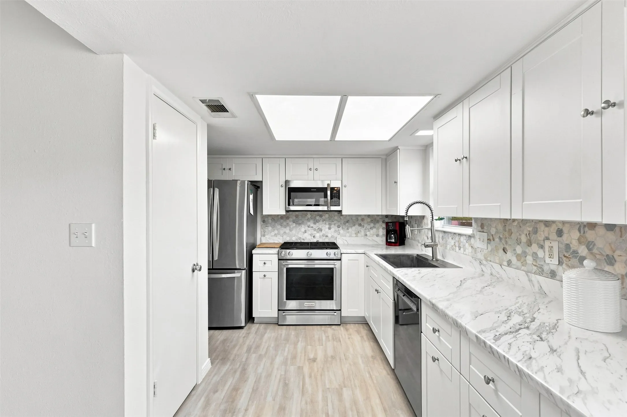 Updated kitchen with white cabinetry, stainless steel appliances, stone-look countertops, and modern backsplash