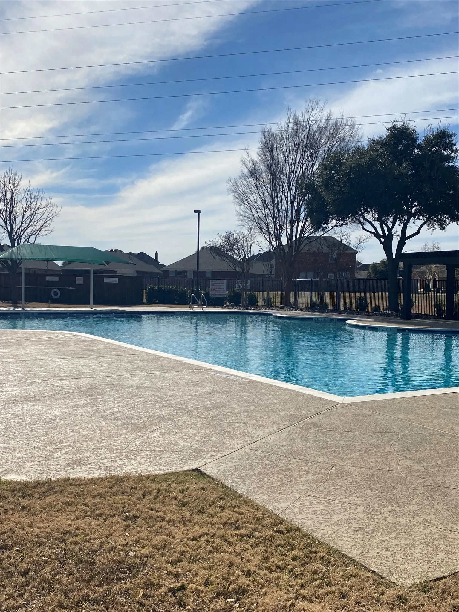 Outdoor swimming pool with integrated tanning ledge, surrounded by stamped concrete decking and a shaded pergola