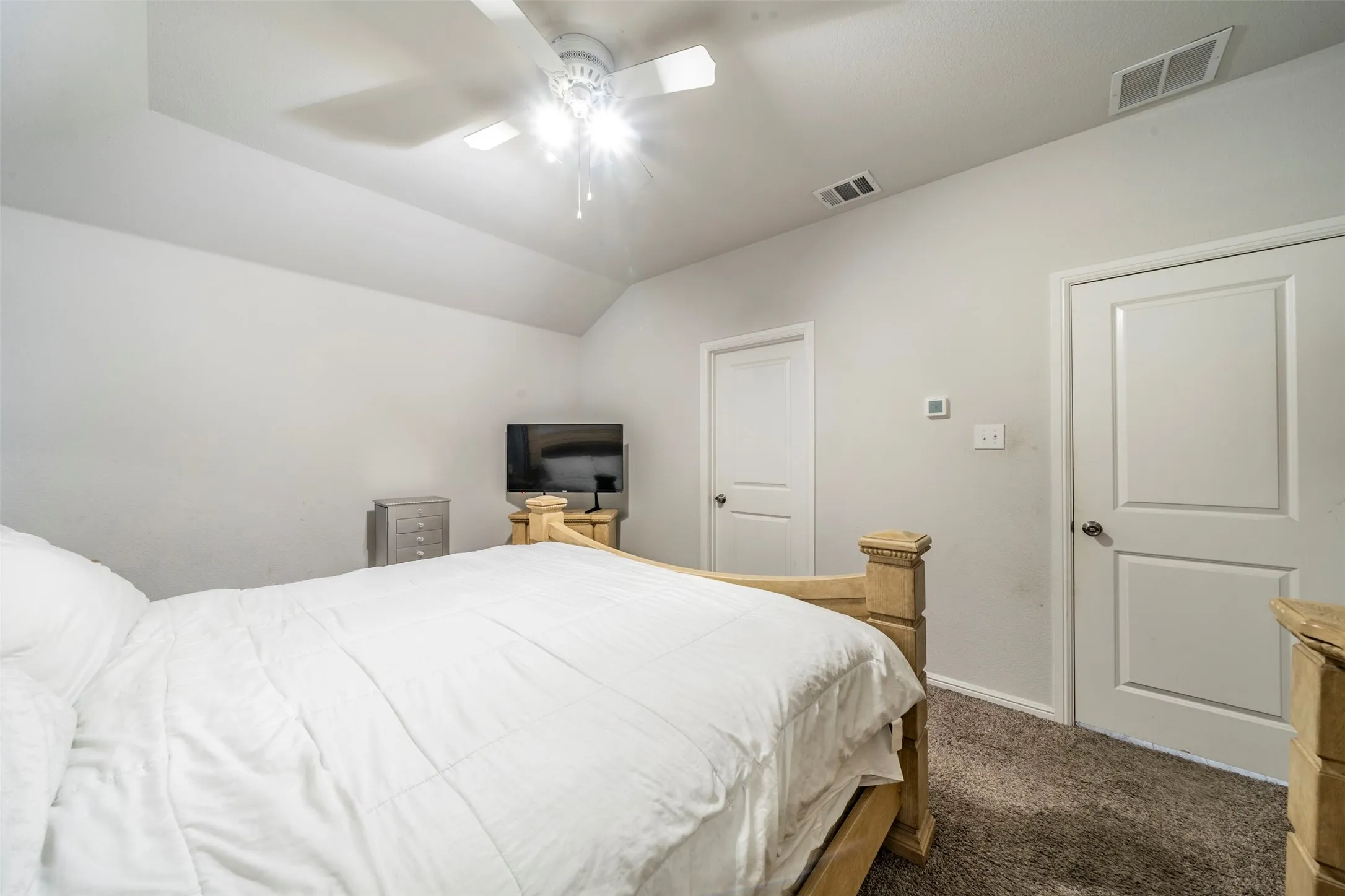 Vaulted ceiling, ceiling fan, neutral wall color, two panel doors, and gray carpet flooring