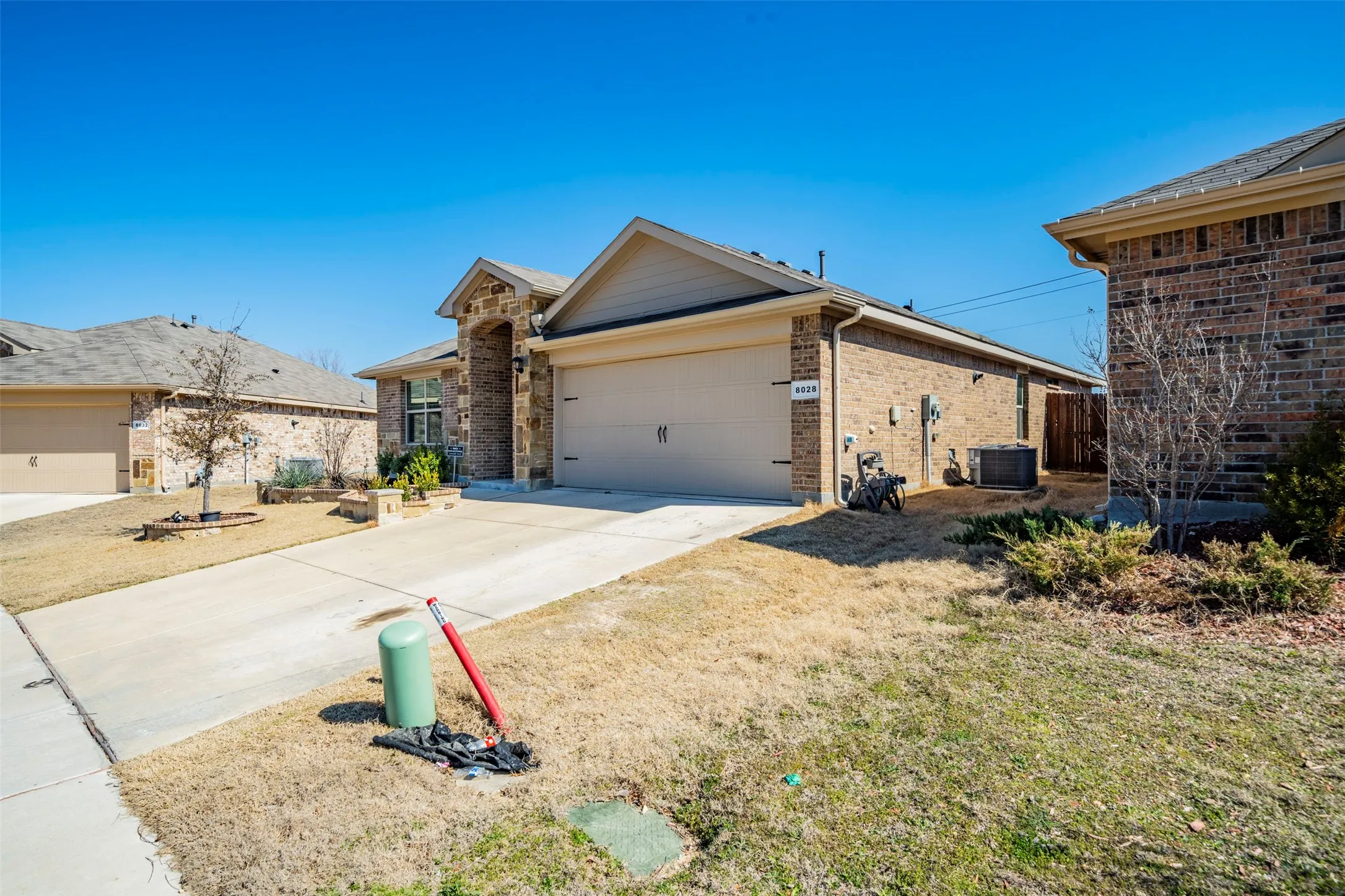Brick and stone exterior, attached garage, concrete driveway, front landscaping, and pitched roof