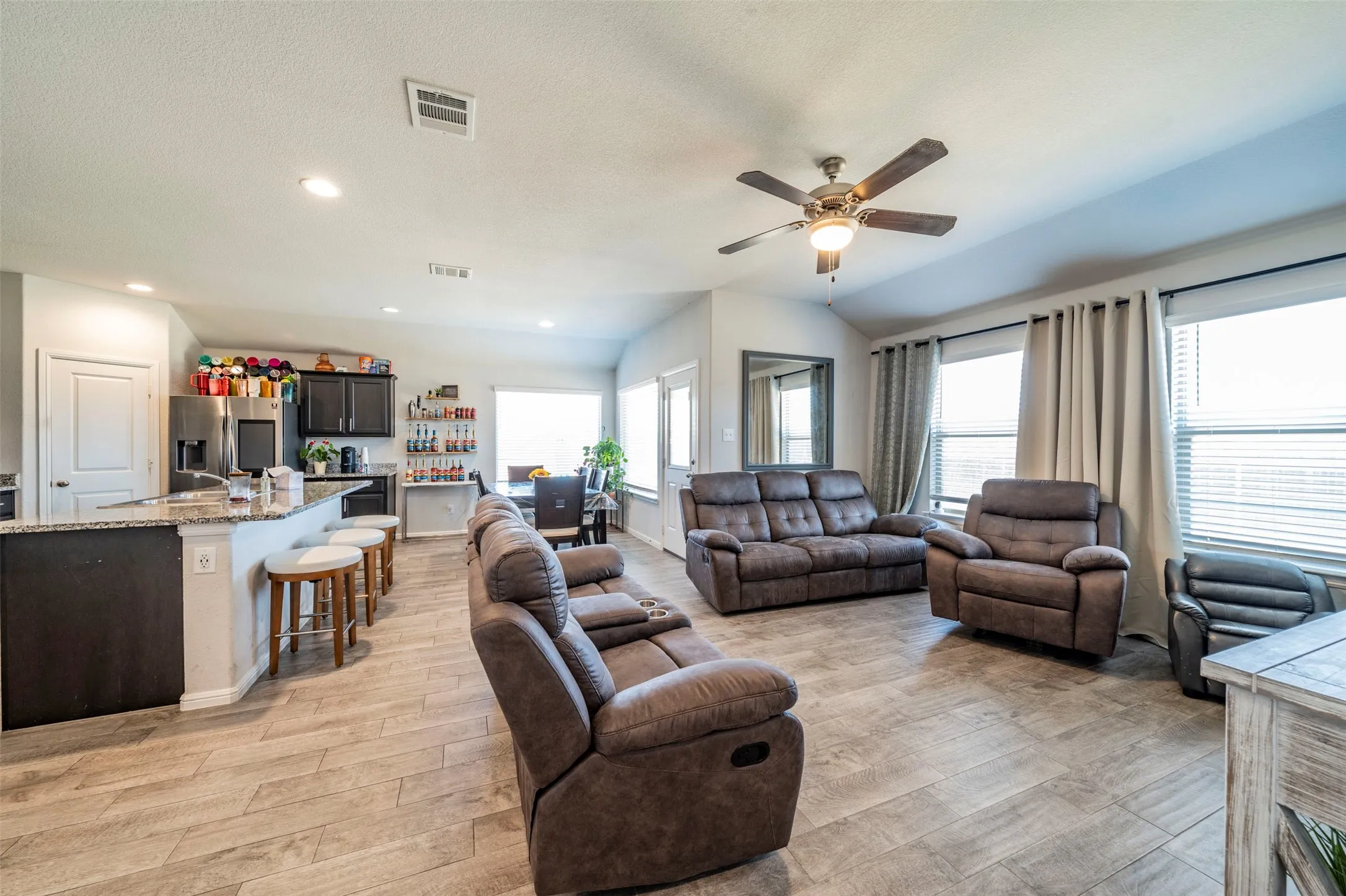 Open-concept living area with wood-finish flooring, a ceiling fan, recessed lighting, and large windows