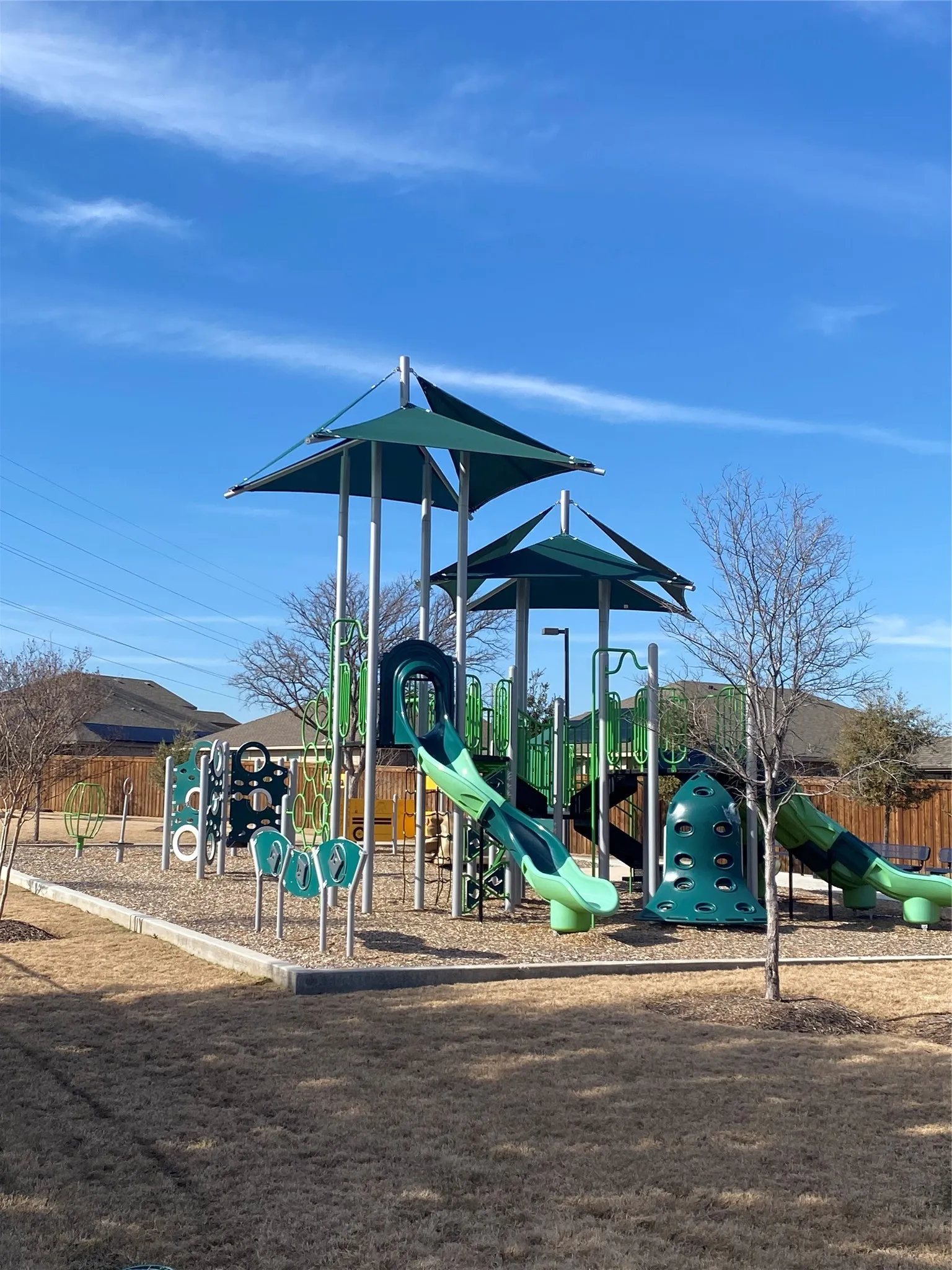 Community playground featuring multiple slides and climbing structures, shade canopies, and a wood chip surface