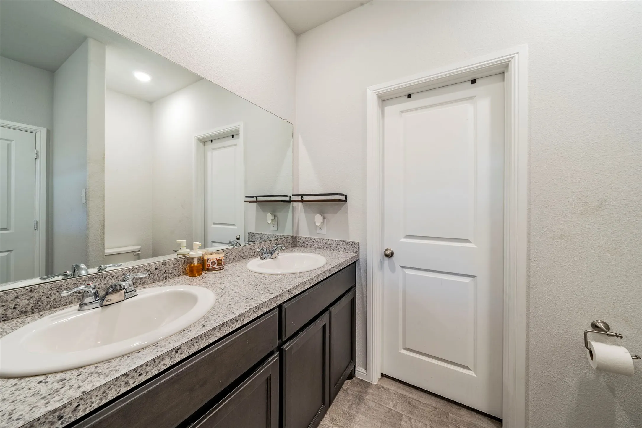 Double vanity with integrated oval sinks, speckled countertop, dark wood-finish cabinetry, and a large wall-mounted mirror