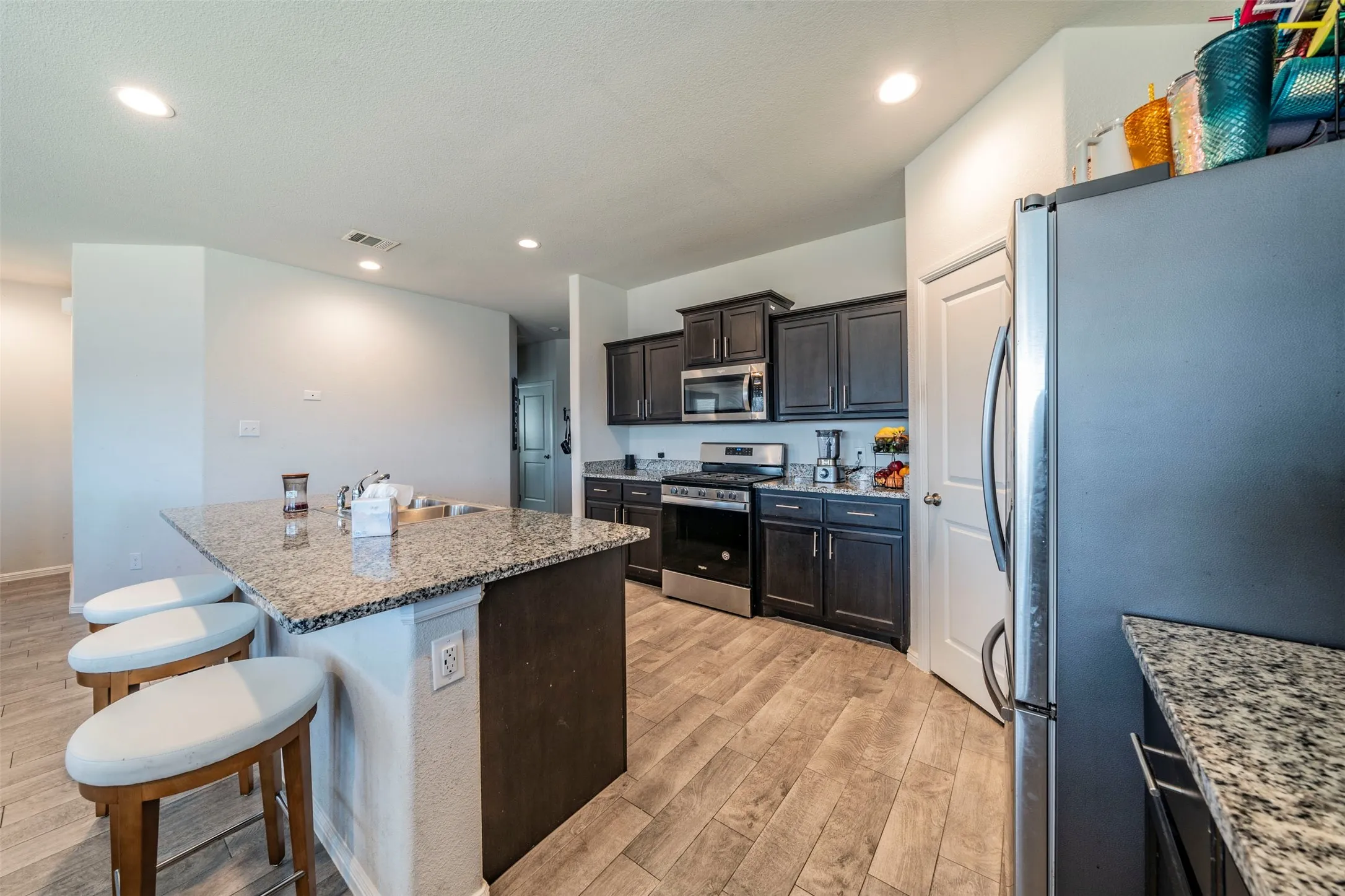 Kitchen featuring a central island with a granite countertop, dark wood-finish cabinetry, stainless steel appliances, and wood-finish flooring