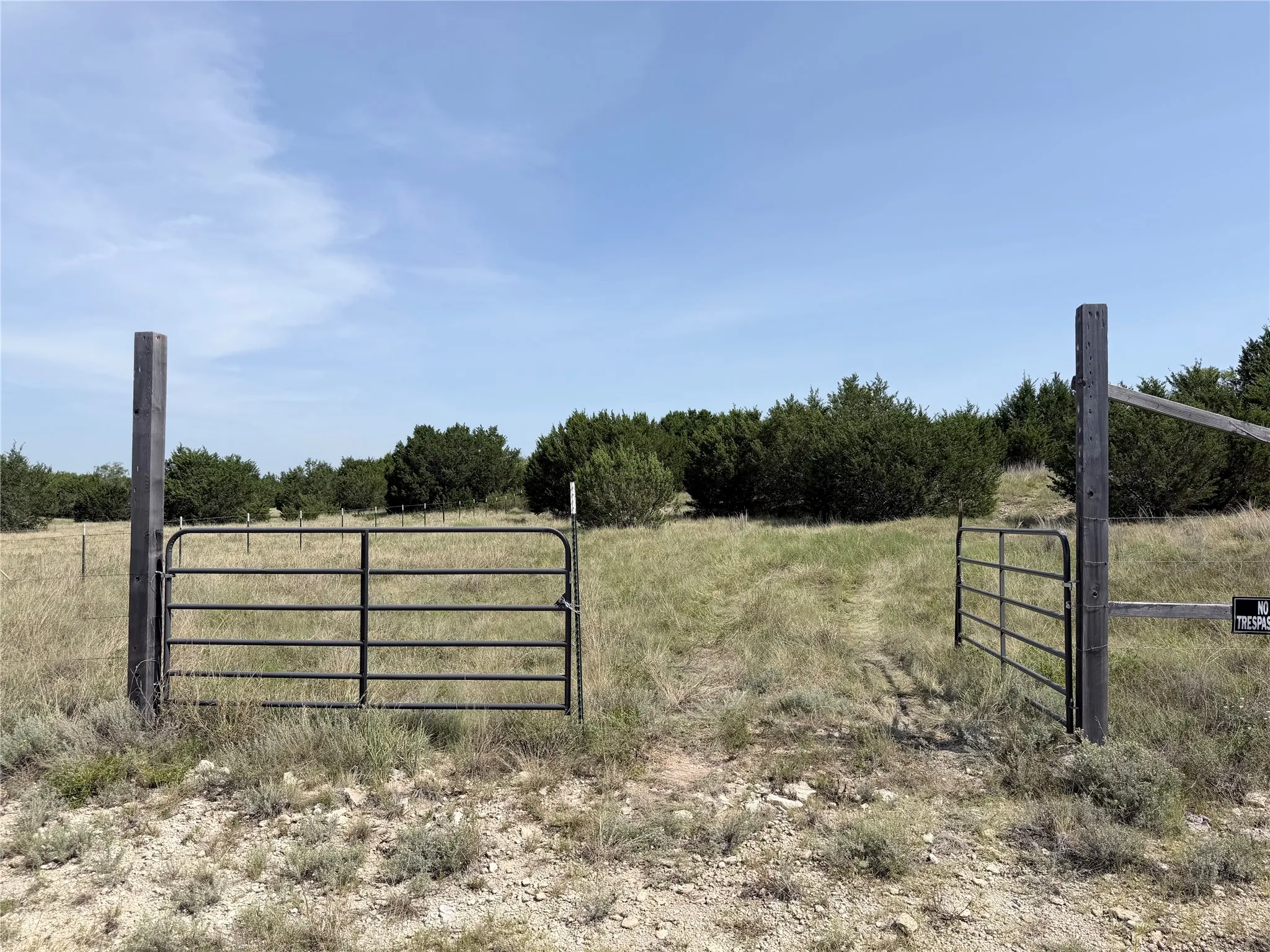 Expansive undeveloped land featuring a partial perimeter fence, natural ground cover, mature trees, and a durable metal gate
