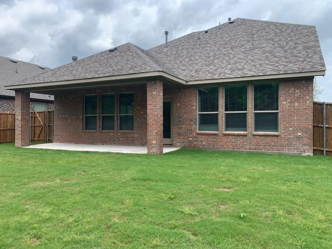 Brick exterior with a covered patio, multiple windows, and a fenced perimeter