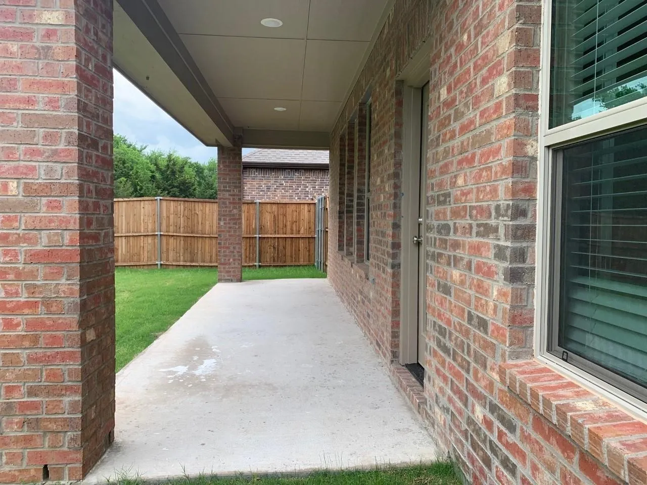 Covered concrete patio with recessed lighting, brick columns, and a wood-slat privacy fence