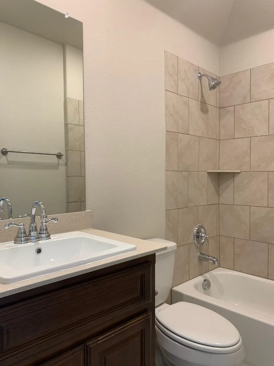 Bathroom featuring a dark wood-finish vanity with an integrated sink, polished chrome fixtures, a full-width mirror, and a tiled shower-over-tub combination with a built-in shelf