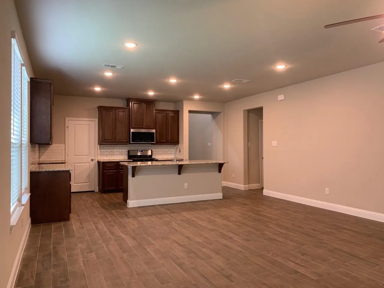 Kitchen with stone countertops, stainless steel appliances, wood-finish flooring, recessed lighting, and a ceiling fan