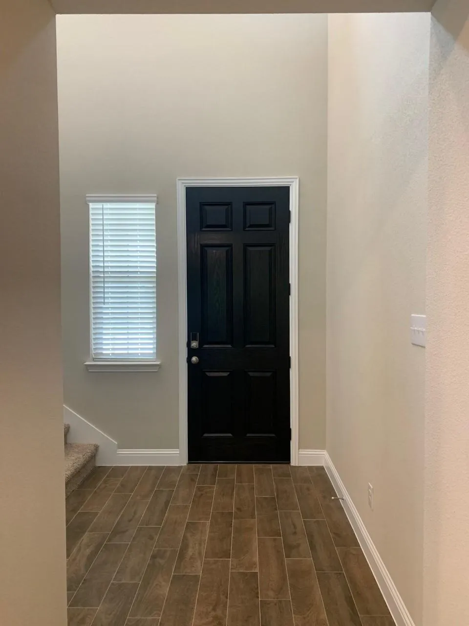 High ceilings with a black paneled door, wood-finish flooring, and white trim