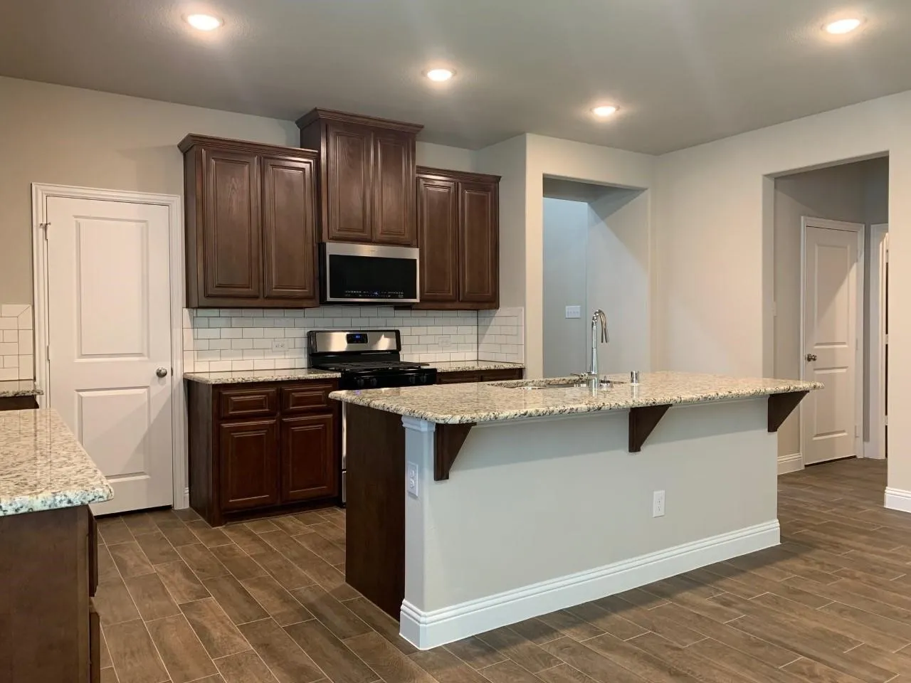 Kitchen featuring wood-finish flooring, dark wood cabinetry, light-toned countertops, subway tile backsplash, and recessed lighting