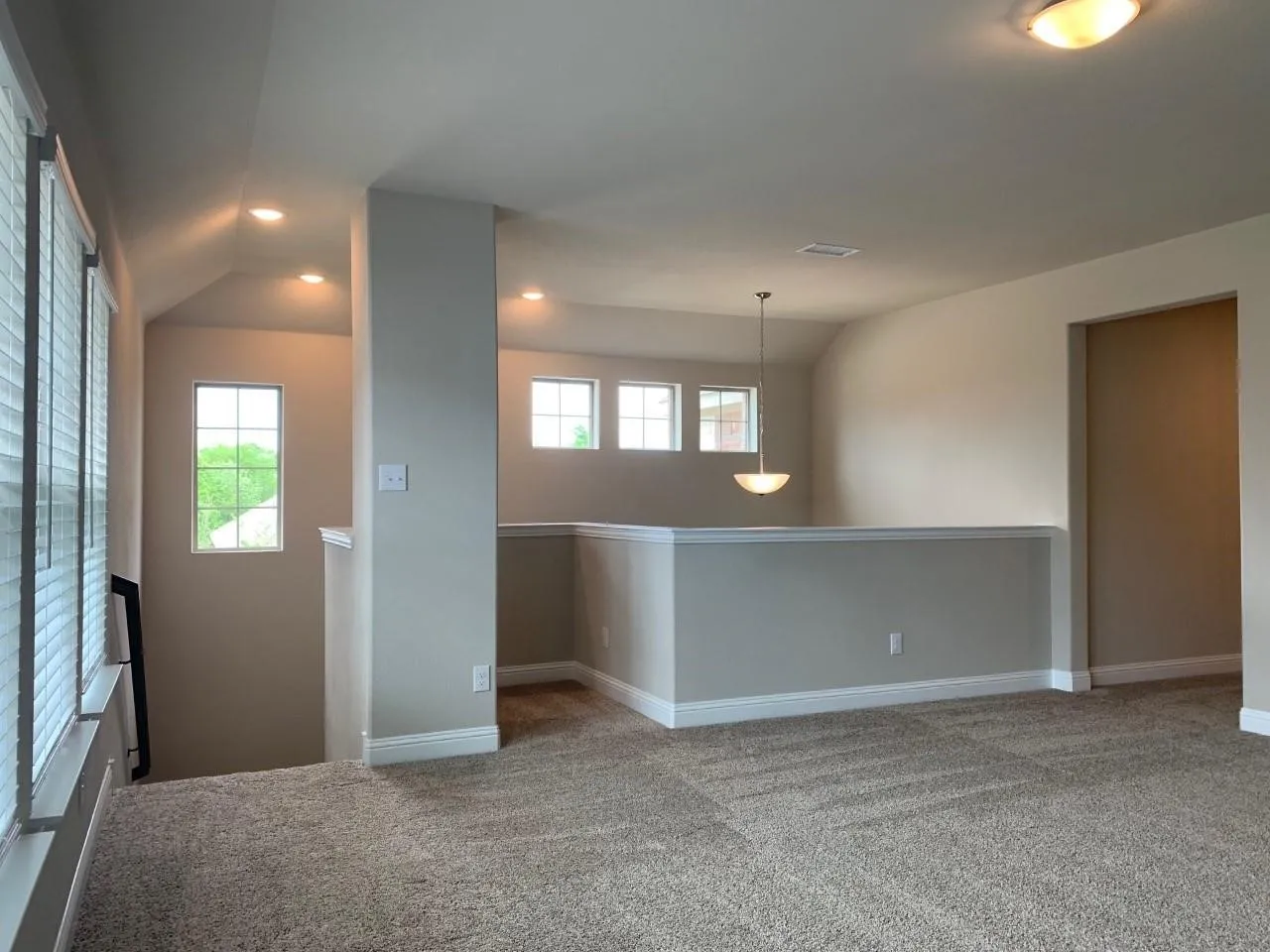 Open loft area featuring carpeted flooring, multiple windows, a ceiling pendant light fixture, and recessed lighting