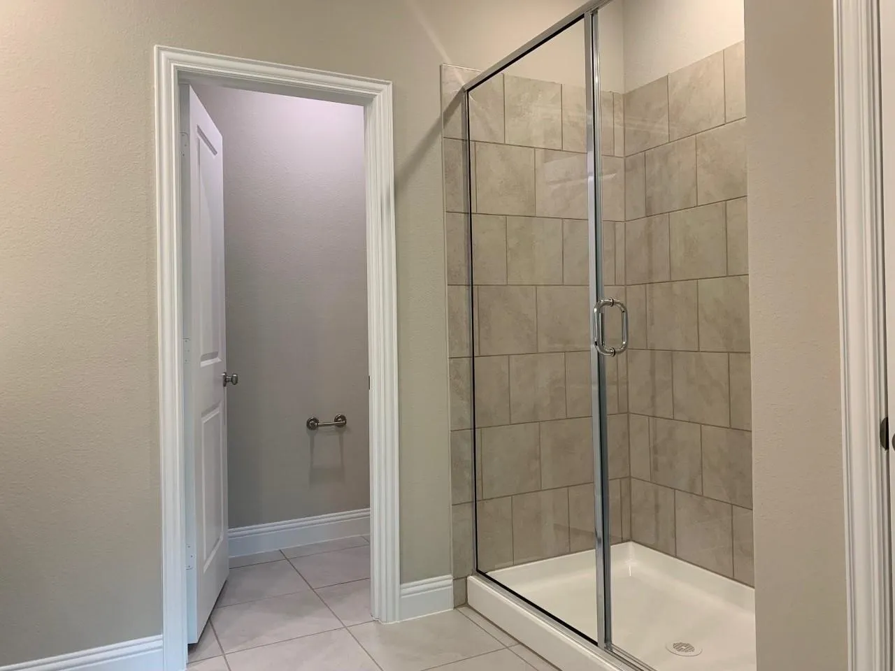 Glass-enclosed shower with tiled walls and a white shower pan