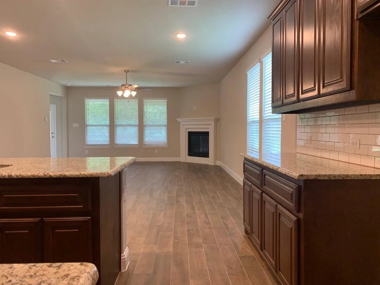 Galley kitchen featuring dark wood cabinetry, granite countertops, subway tile backsplash, and wood-finish flooring throughout