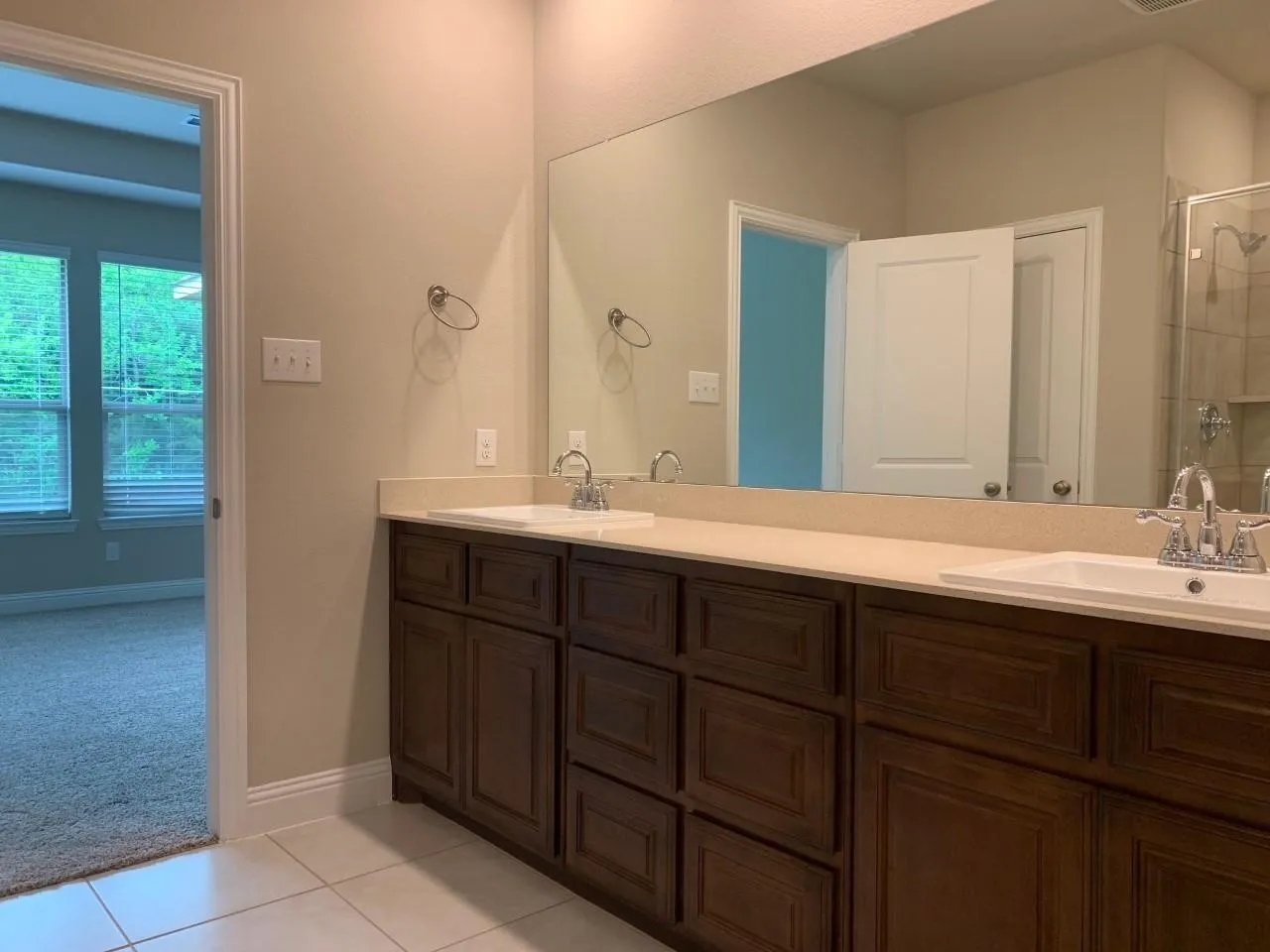 Dual vanity with wood-finish cabinetry, light-toned countertop, and integrated sinks