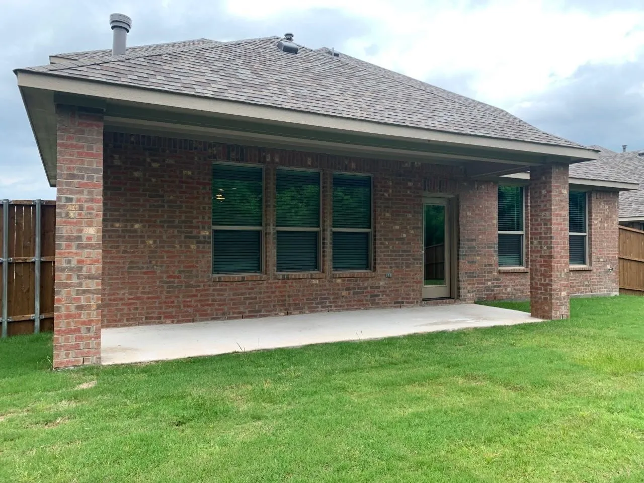 Brick exterior with a covered patio, concrete slab, and wood-paneled fencing