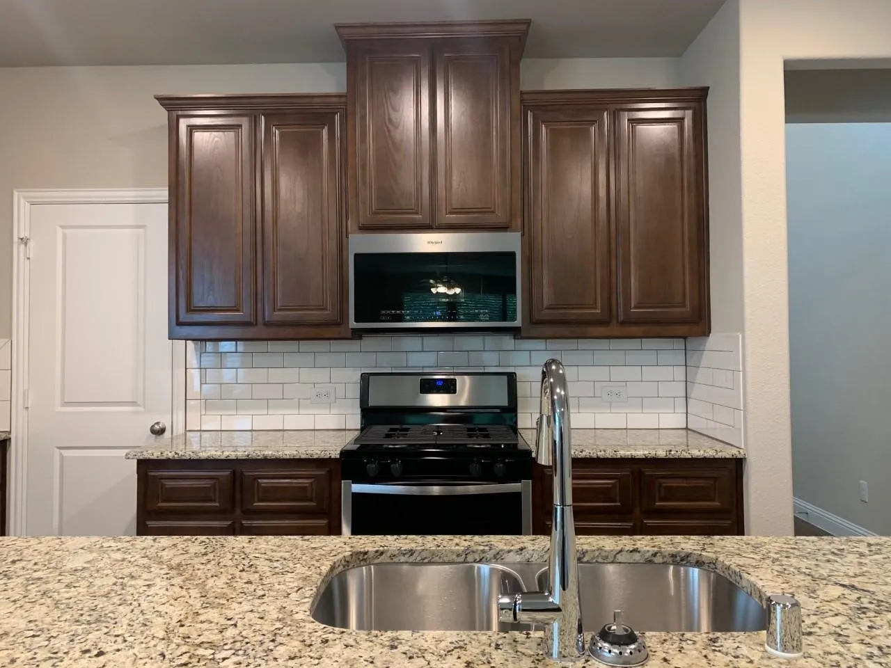 Granite countertops, stainless steel appliances, wood-finish cabinetry, subway tile backsplash, and a double basin sink