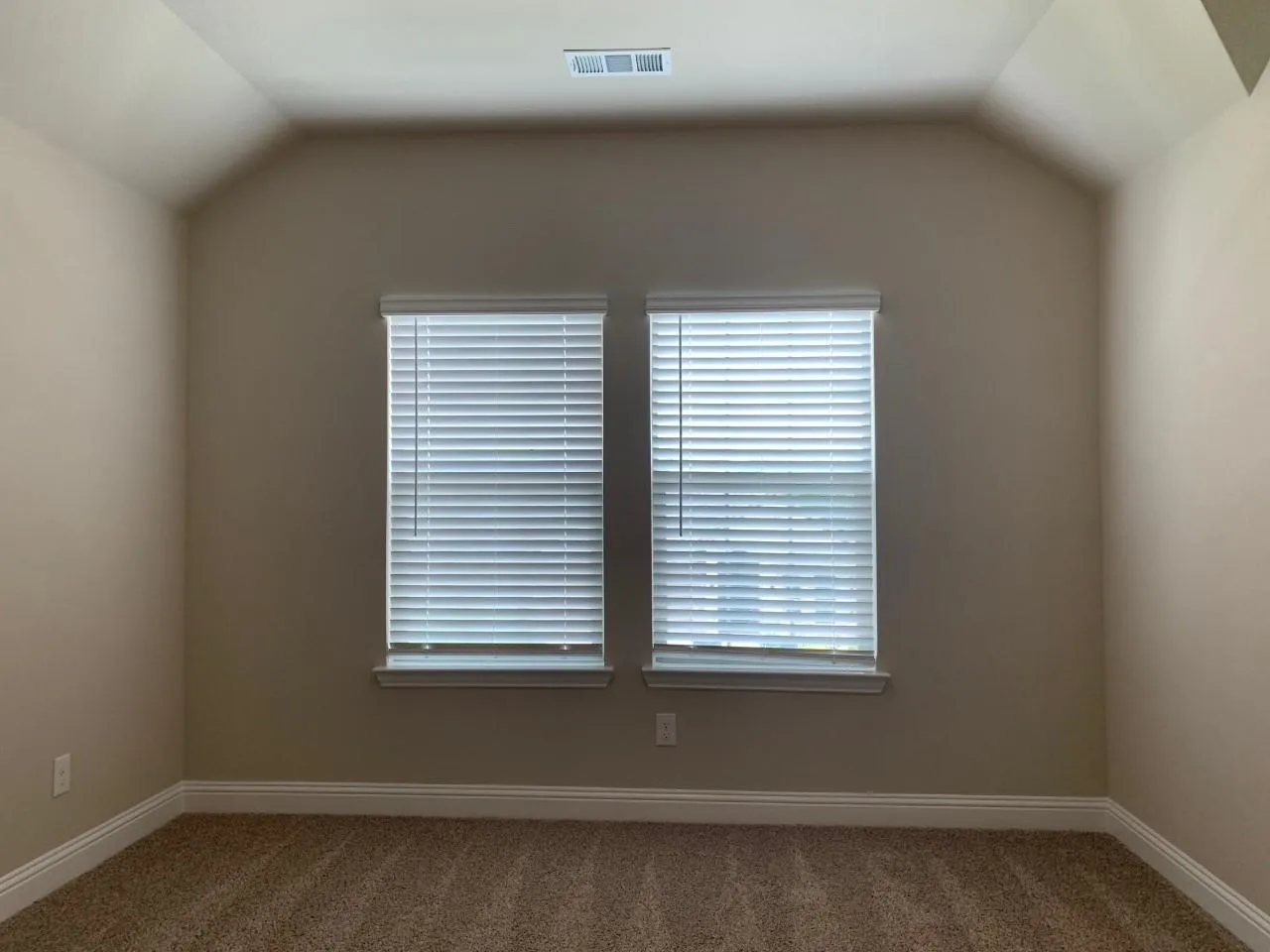 Vaulted ceiling with a central vent, two windows with blinds, neutral-toned walls, and carpet flooring
