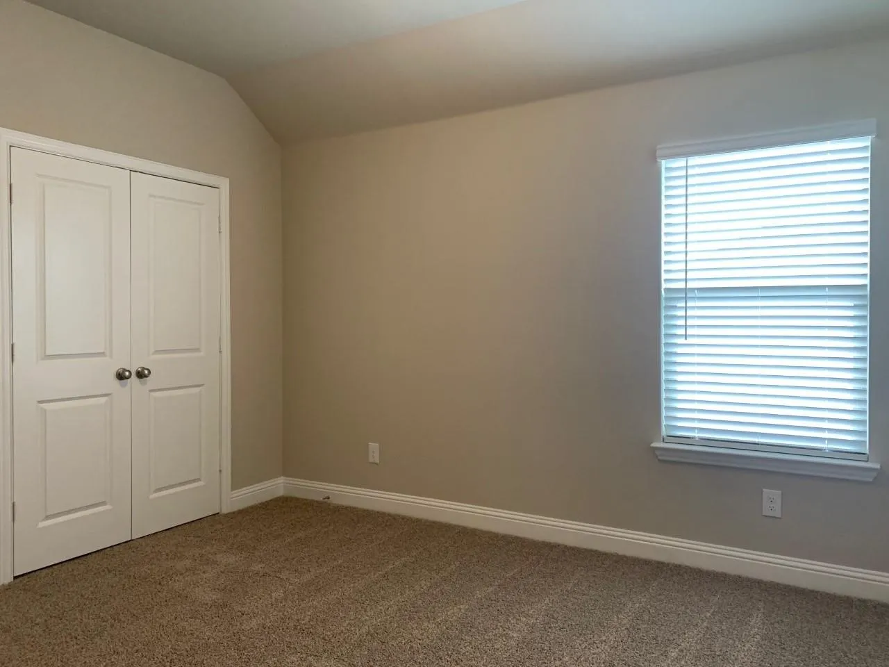 Carpeted room with a vaulted ceiling, white trim, a double-door closet, and a window with blinds