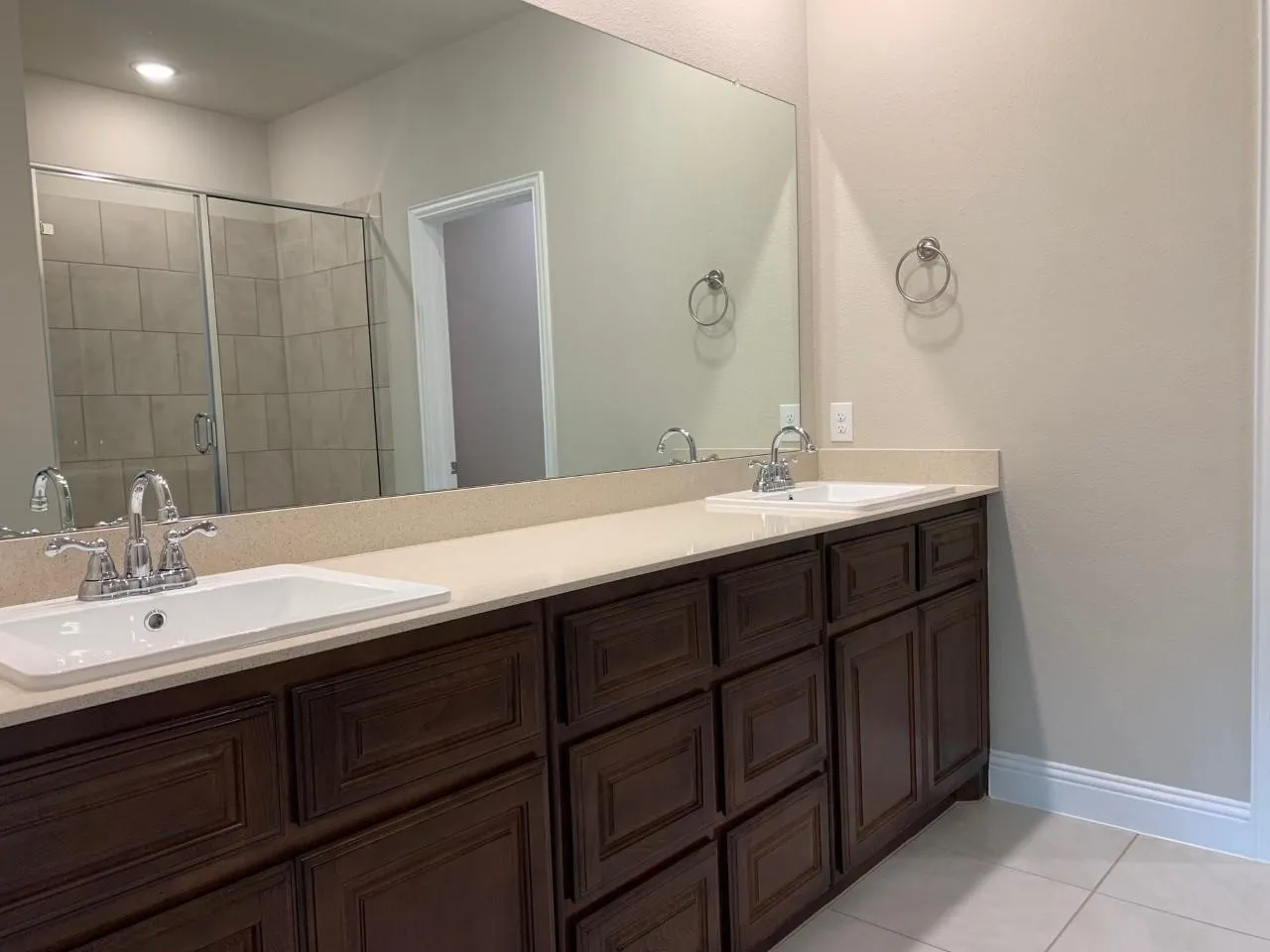 Dual vanity with integrated sinks, expansive countertop, dark wood-finish cabinetry, and tiled flooring