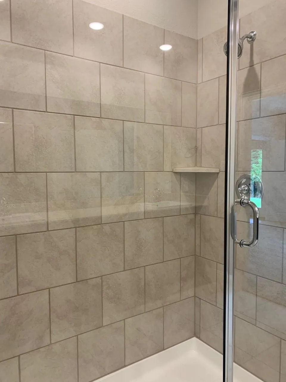 Shower enclosure featuring large format tile walls, a built-in corner shelf, a clear glass door, chrome hardware, and recessed lighting