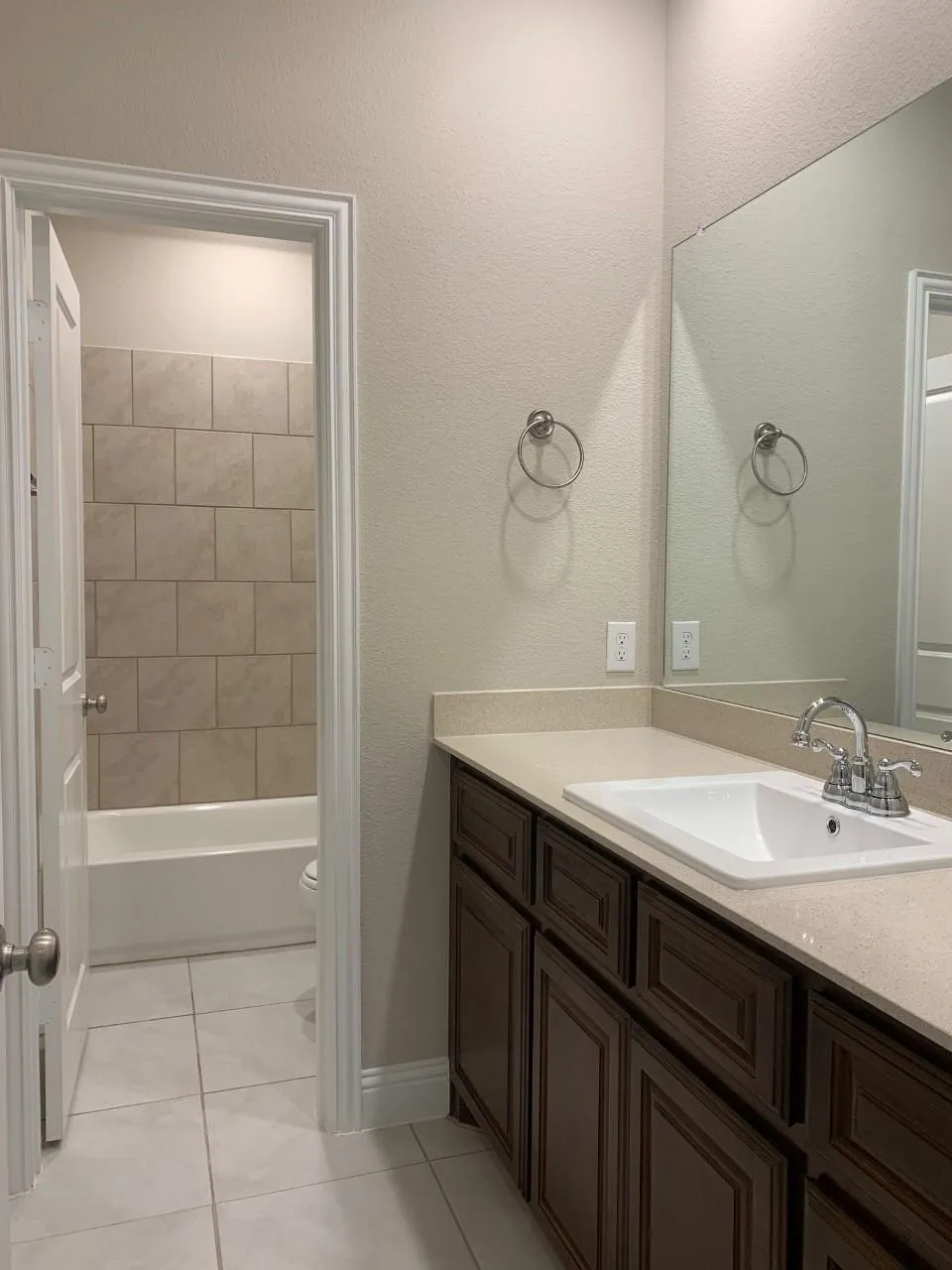 Vanity with an integrated sink and light-colored countertop, dark wood-finish cabinetry, chrome faucet, and a large wall-mounted mirror