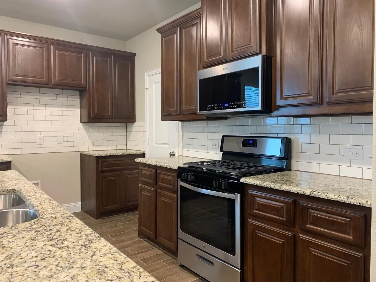Kitchen featuring granite countertops, a subway tile backsplash, dark wood-finish cabinetry, stainless steel appliances, and wood-finish flooring