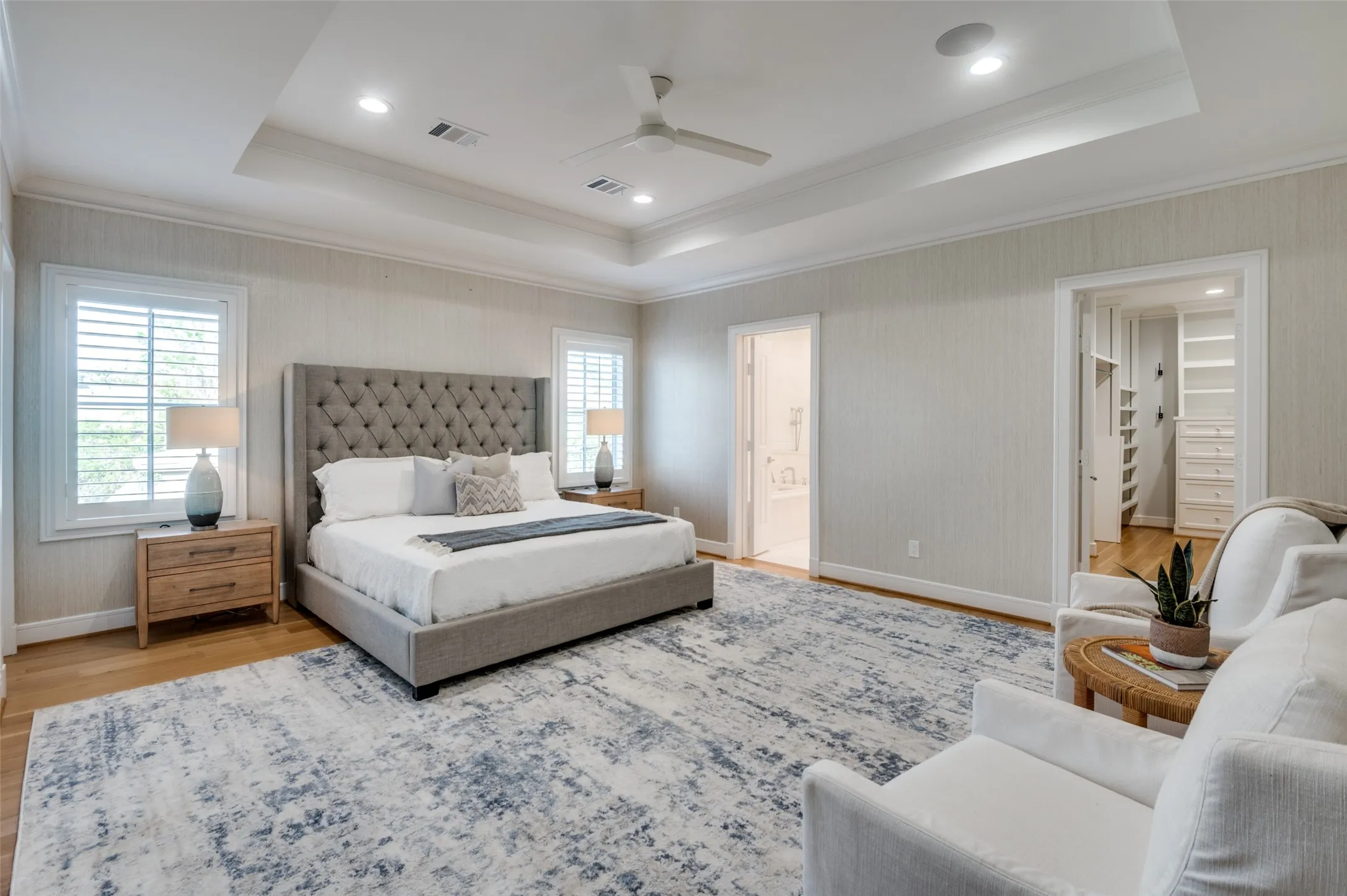 Tray ceiling with recessed lighting and ceiling fan, wood-finish flooring, two large windows with plantation shutters, and a built-in closet system