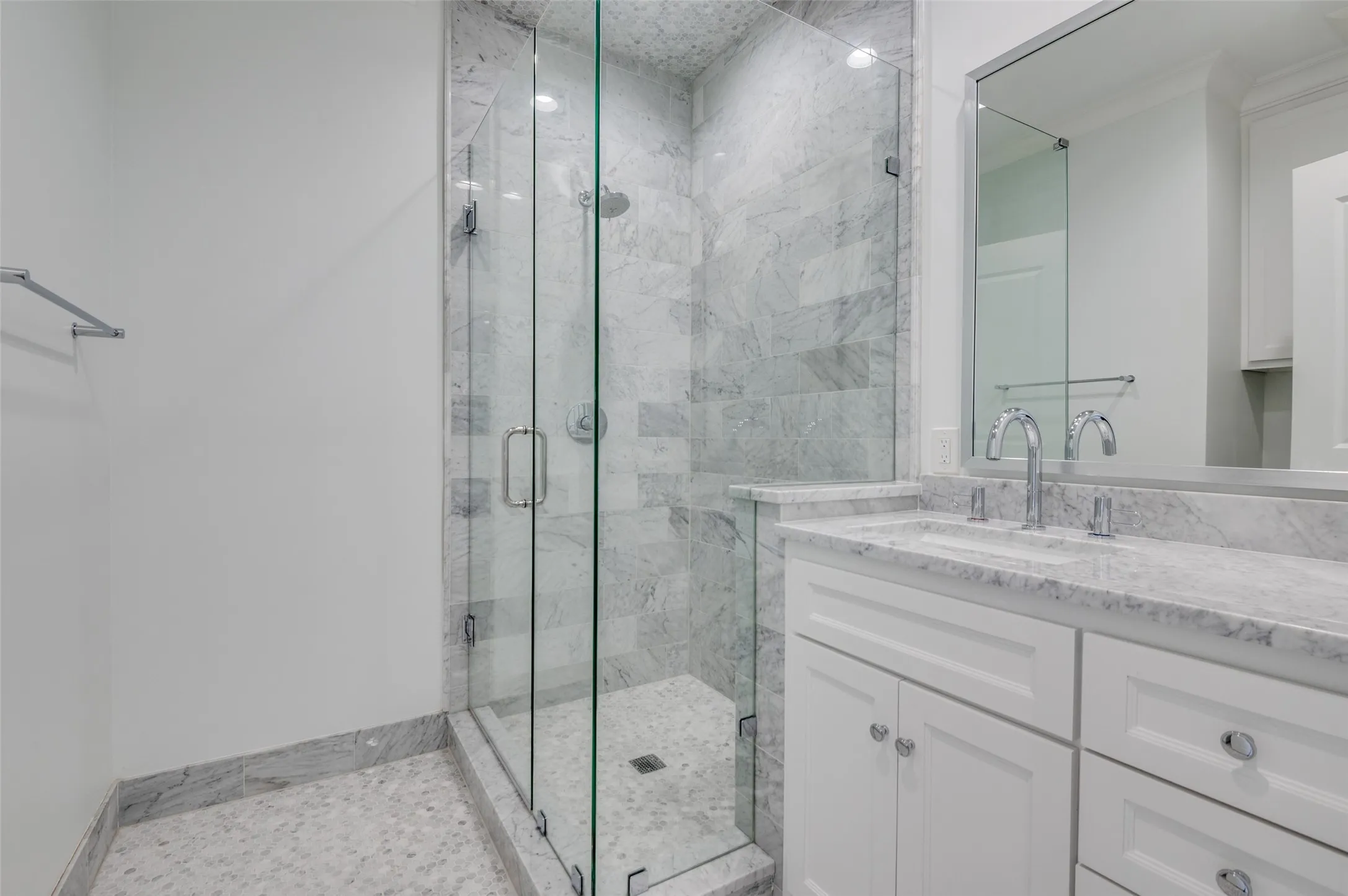 Glass-enclosed shower with full-height tile surround, dual-handle shower fixtures, vanity with undermount sink, countertop, and framed mirror