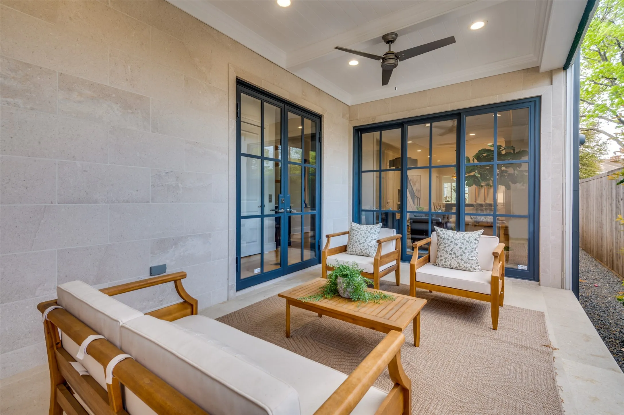 Covered outdoor patio featuring light-toned stone block exterior, ceiling fan with integrated lighting, recessed lighting, and expansive glass panel doors