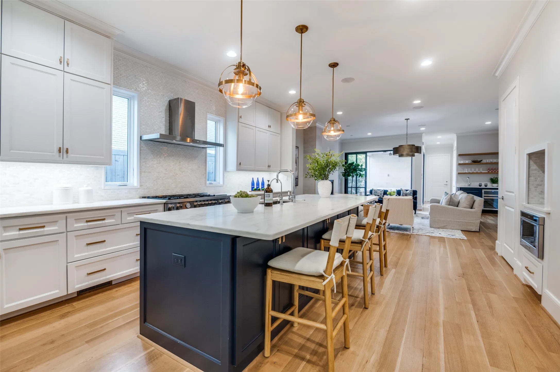 Gourmet kitchen with a large center island, white cabinetry, integrated range hood, and light wood-finish flooring