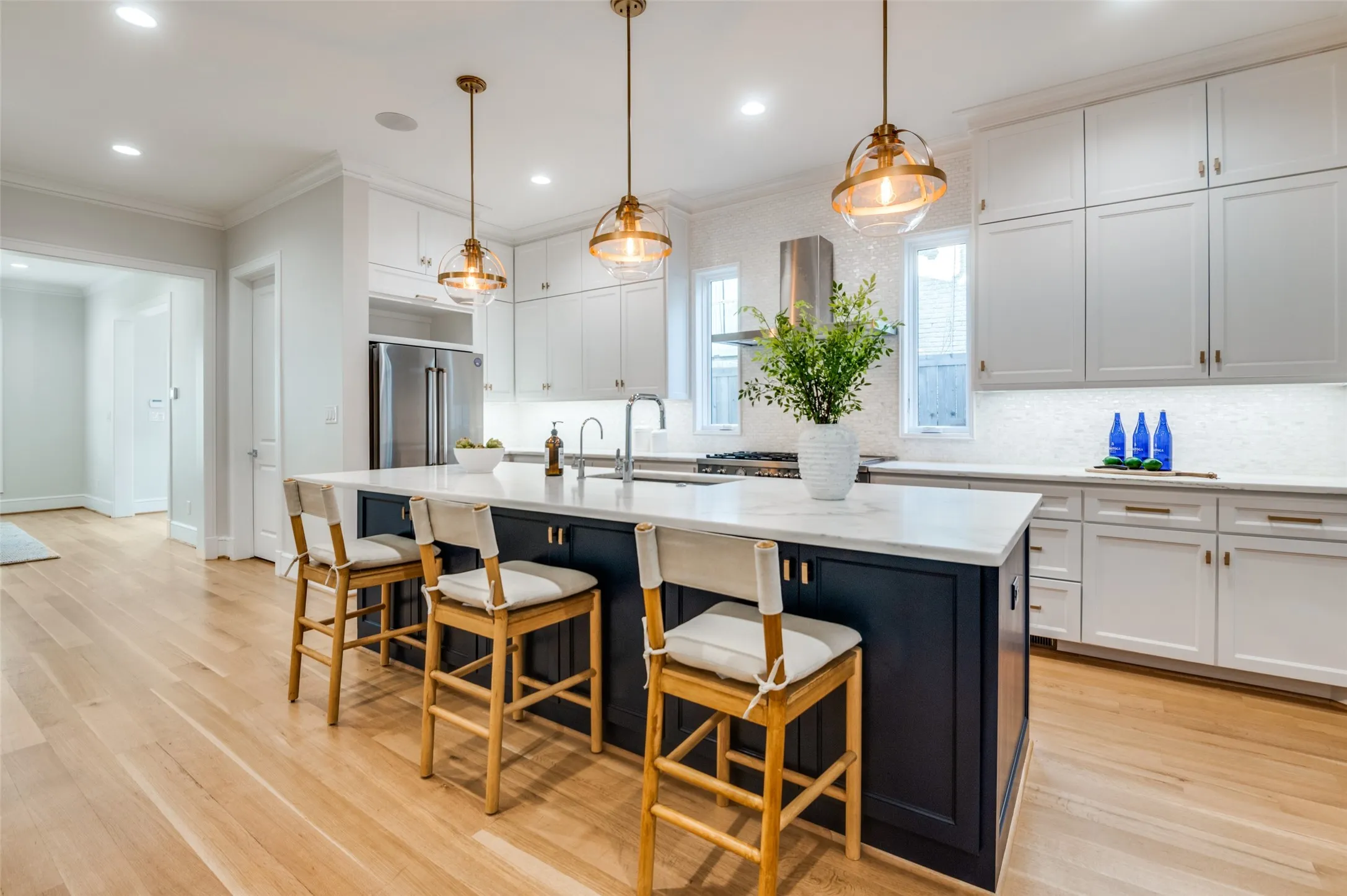 Spacious kitchen featuring an expansive center island with seating, stainless steel appliances, light-toned wood-finish flooring, white upper and lower cabinetry, and a tile backsplash