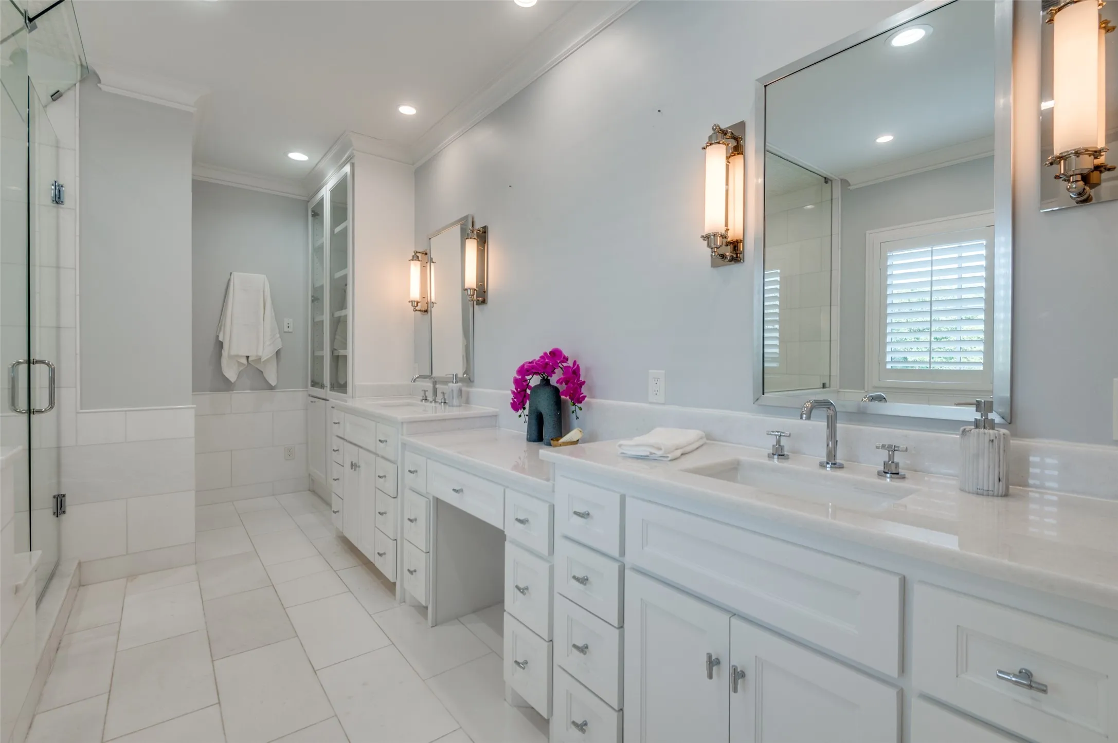Expansive bathroom featuring dual vanity sinks, extensive white cabinetry, a glass-enclosed shower, and built-in storage
