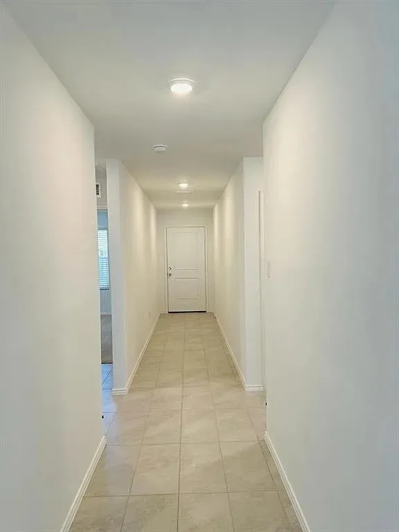 Recessed lighting illuminates the hallway with tile flooring and neutral wall finishes