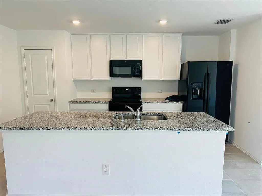 Kitchen featuring an island with a dual basin stainless steel sink, light-colored speckled countertops, white upper and lower cabinetry, a black range, and a black refrigerator