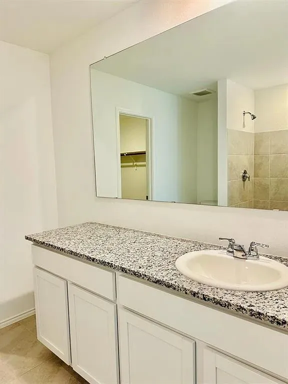 White vanity with a speckled countertop, undermount sink, and chrome faucet