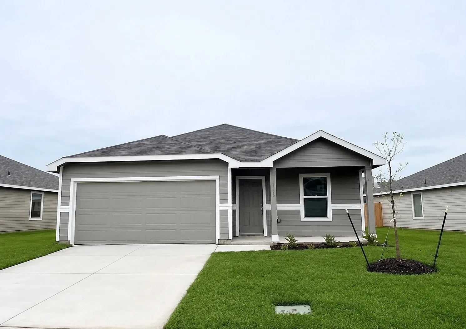 Single-story residence featuring gray siding with white trim, an attached garage, a paved driveway, and a front entry door with a covered porch
