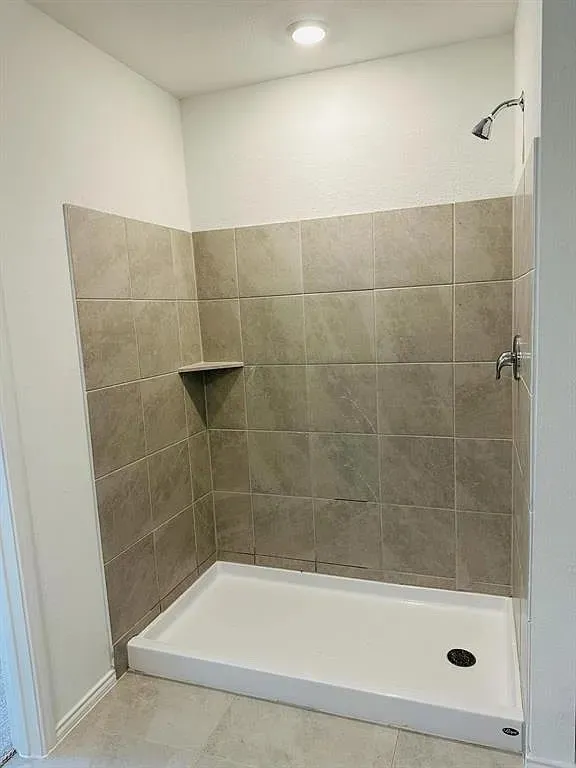 Tiled shower with a built-in shelf, chrome showerhead, and white shower pan