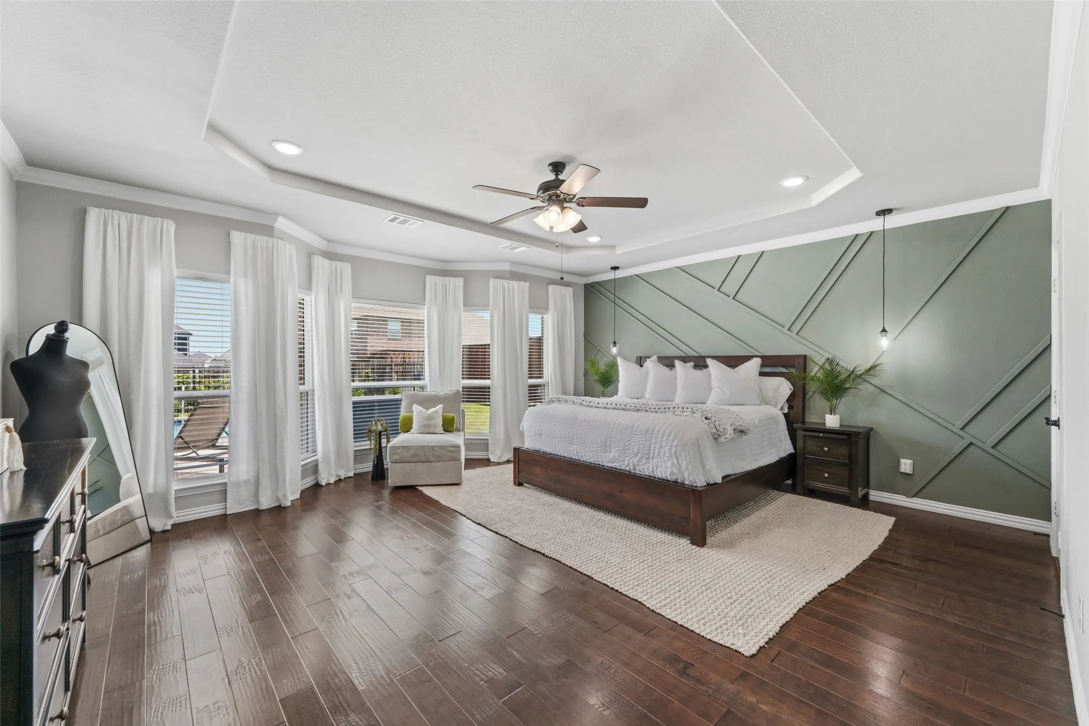 Wood-finish flooring, accent wall with geometric molding, tray ceiling with recessed lighting, ceiling fan, and multiple windows