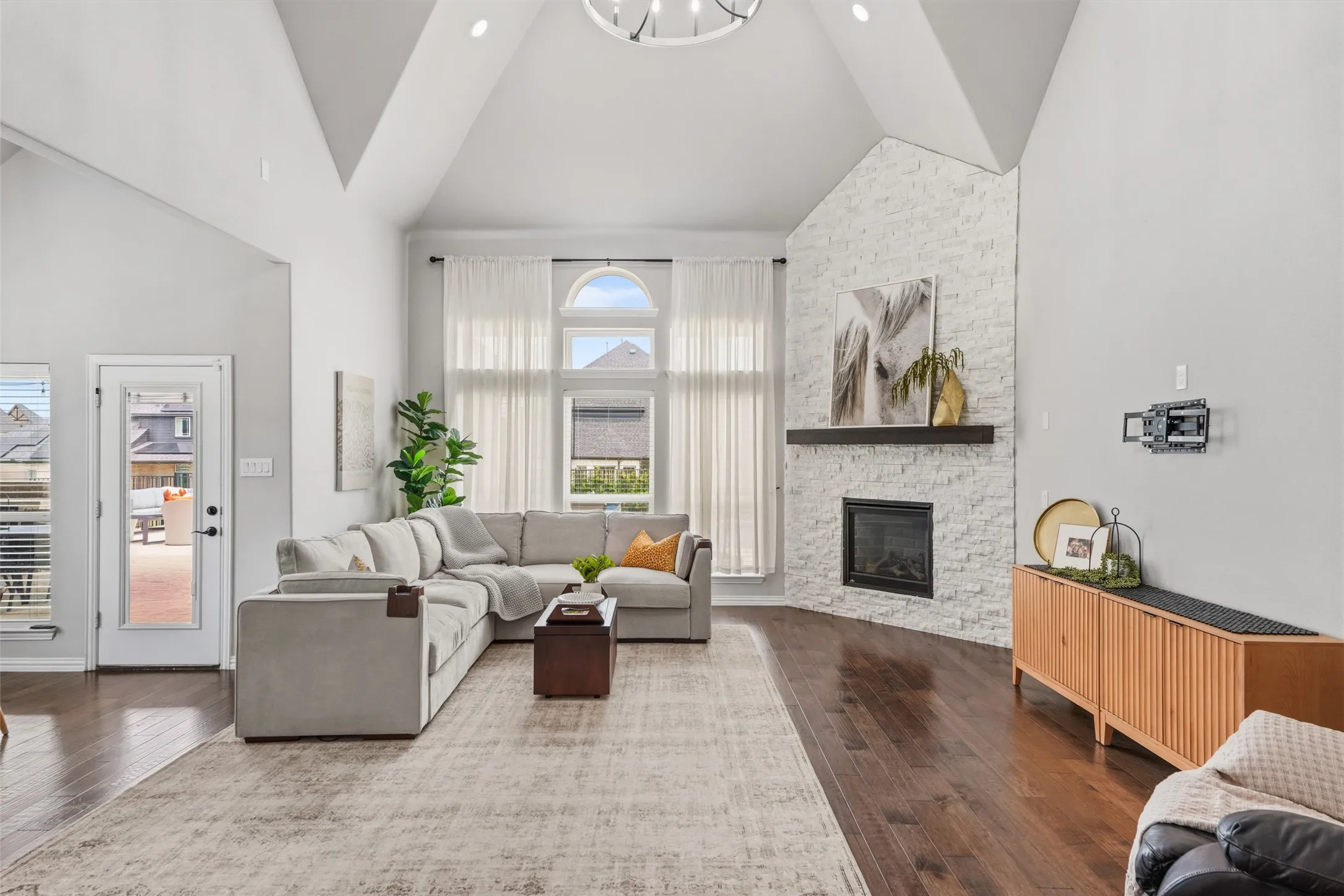 Soaring vaulted ceilings with skylights illuminate this open-concept living space, featuring a wood-burning fireplace with white subway tile surround and wood mantel