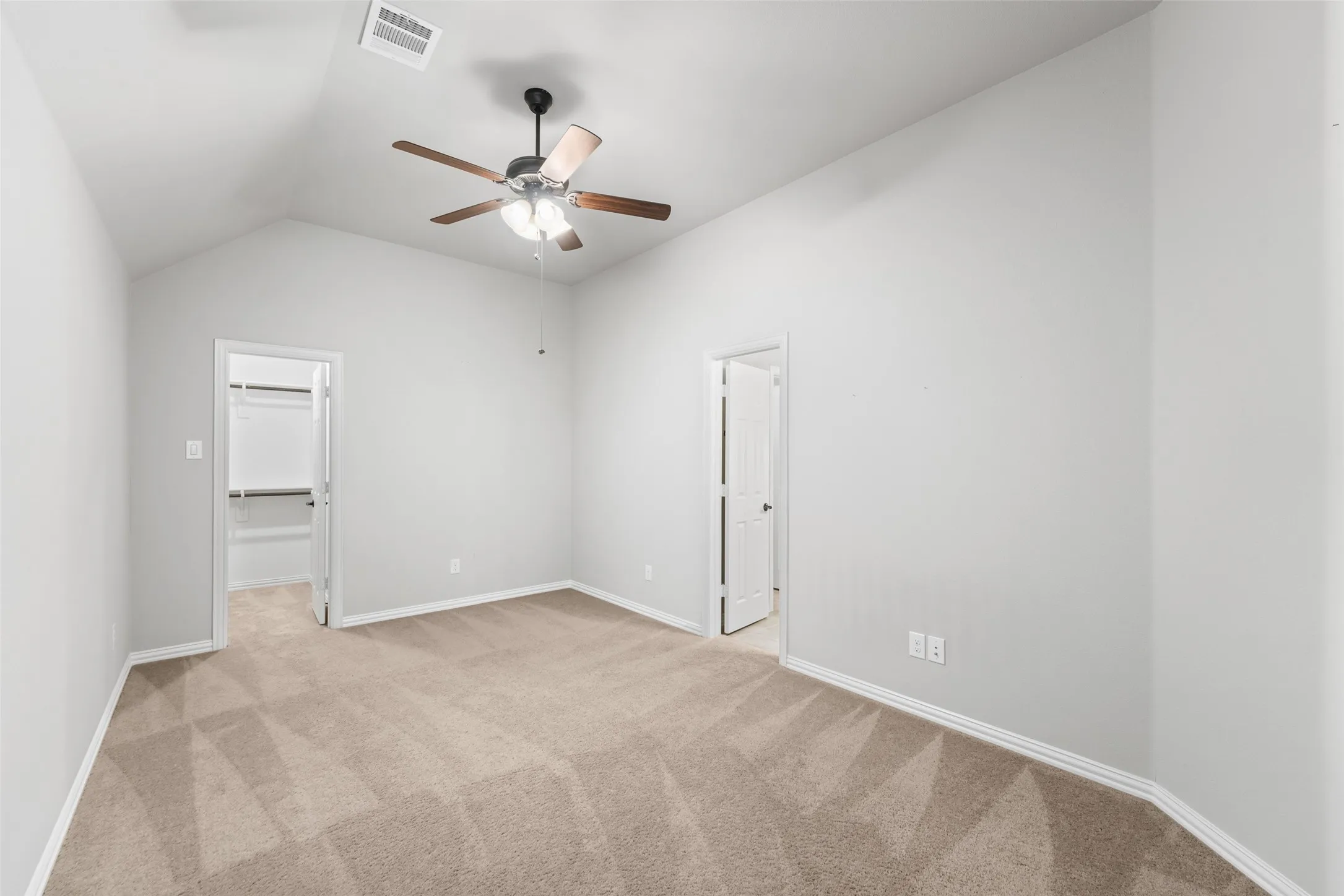 Vaulted ceiling, ceiling fan with light fixture, neutral carpet flooring, and a walk-in closet with shelving